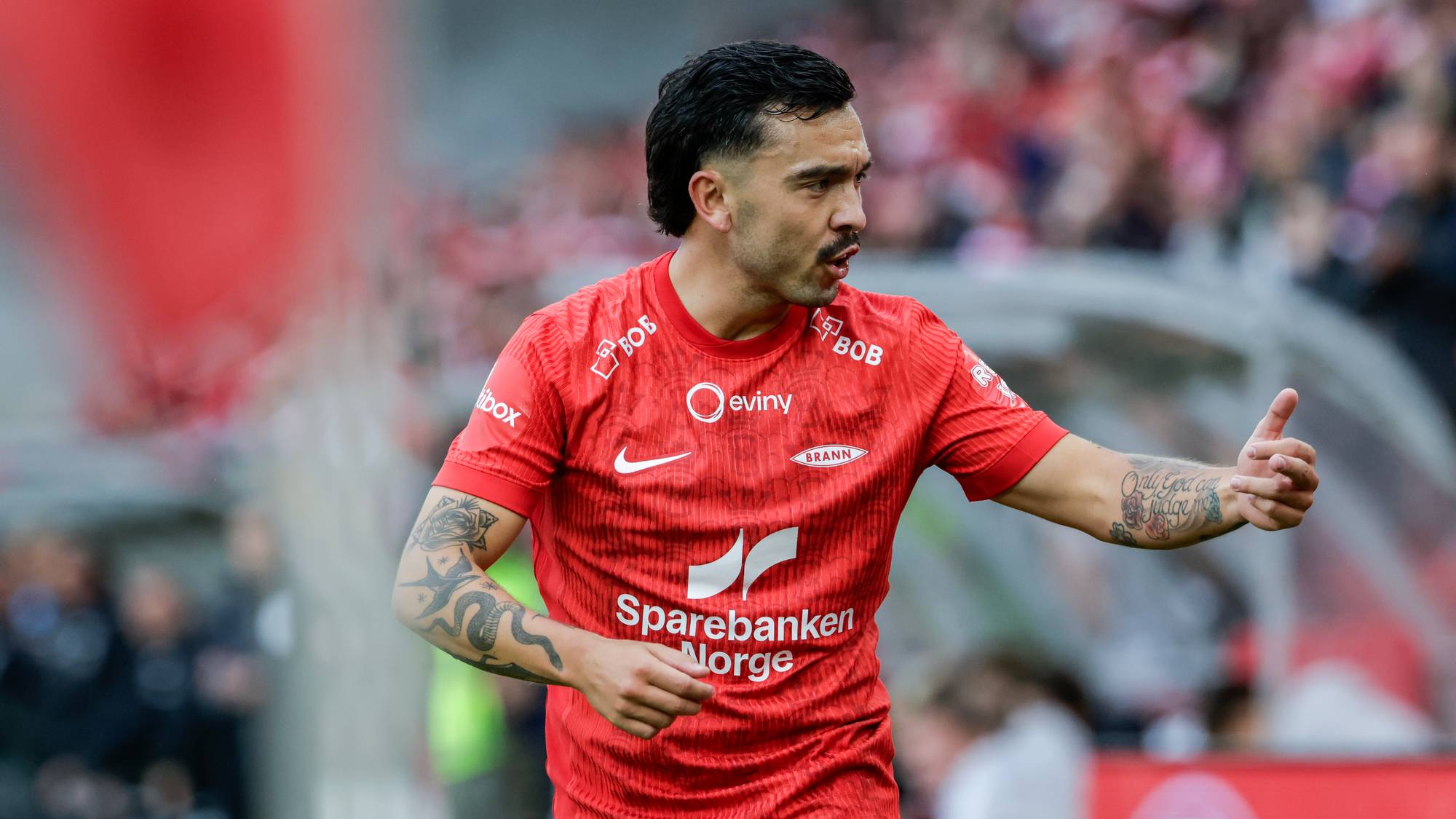Fotballspiller fra Brann i rød drakt på banen under kamp. (Bildebeskrivelsen er laget av en KI-tjeneste)