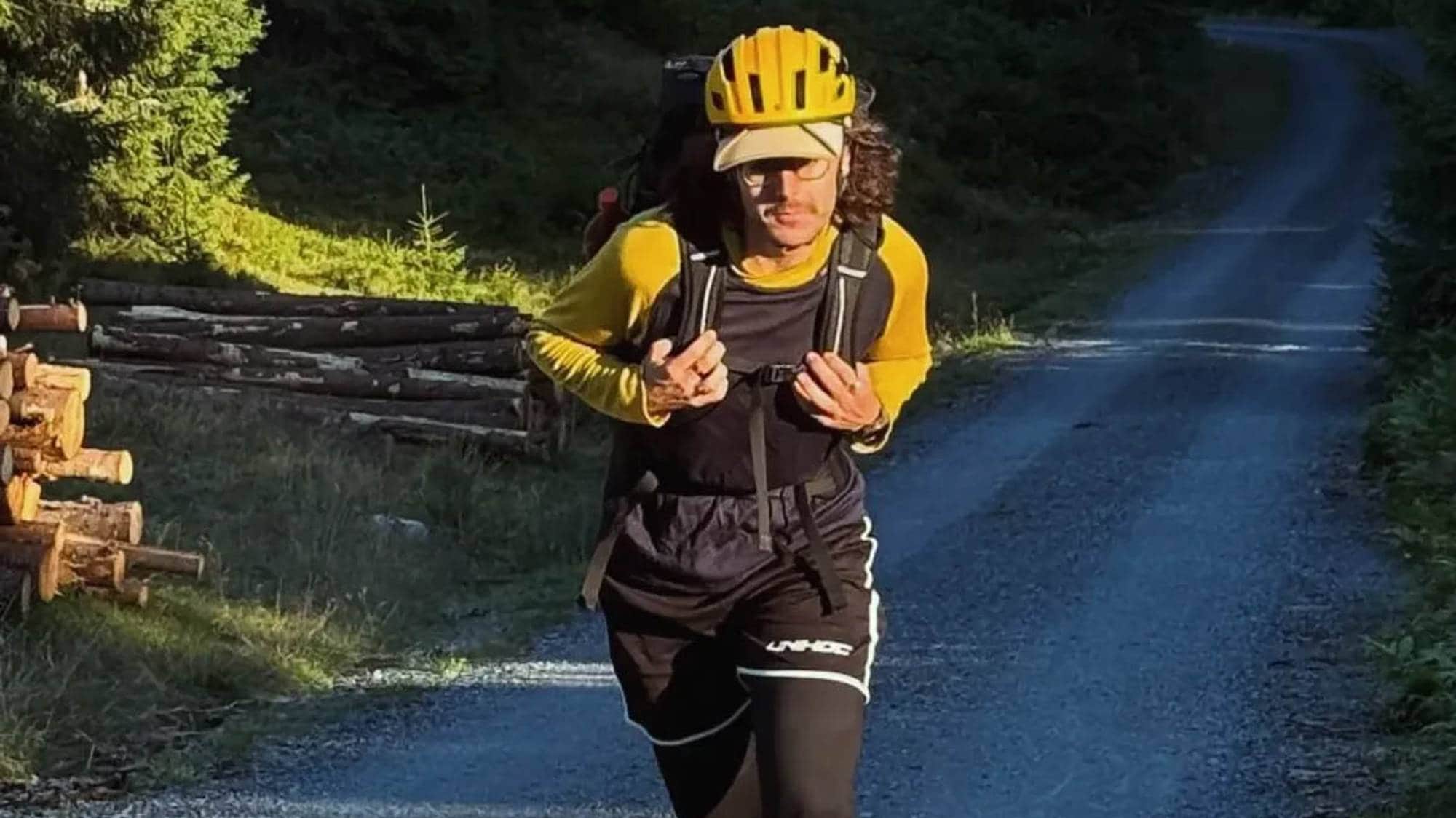En person med gul hjelm og genser med gule ermer skøyter på rulleskøyter langs en grusvei i en skog.