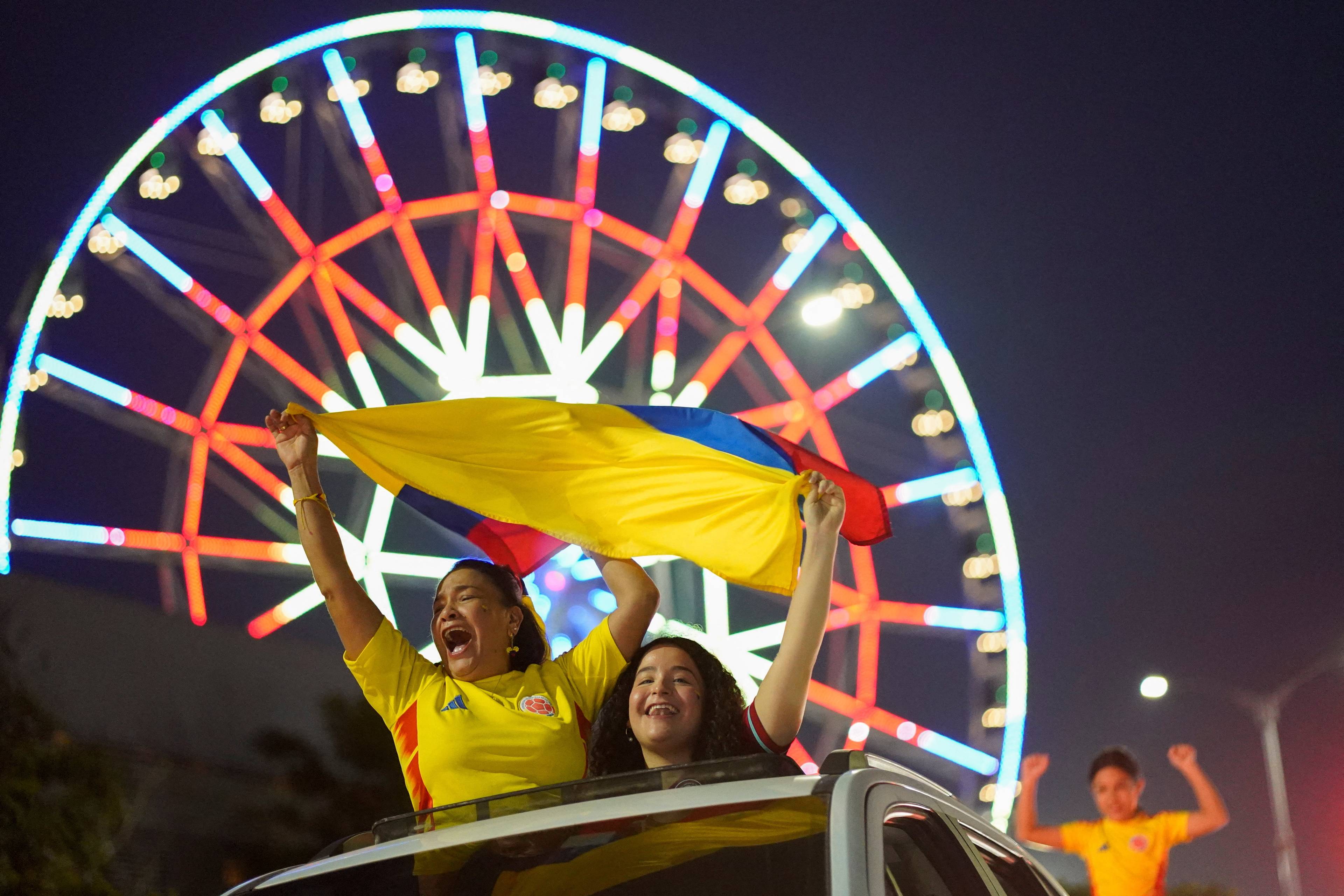To personer vifter med det colombianske flagget fra et bilvindu. I bakgrunnen vises et pariserhjul med lys. (Bildebeskrivelsen er laget av en KI-tjeneste)