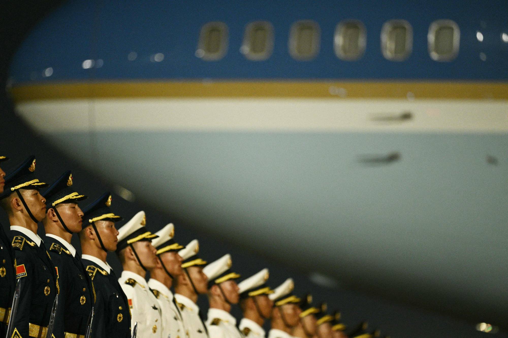 Militært personell i uniform står på rekke foran et fly. En vannrett gul stripe går langs flykroppen. Vinduene på flyet er synlige i bakgrunnen. (Bildebeskrivelsen er laget av en KI-tjeneste)