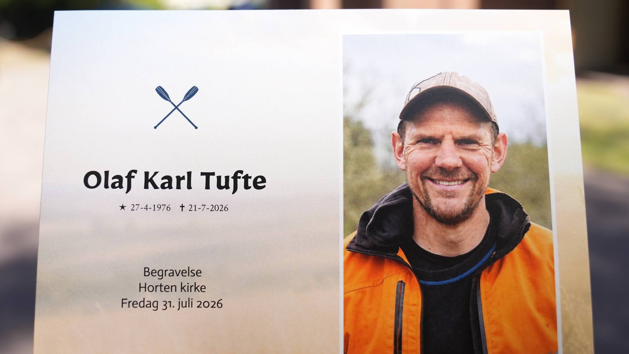 Hånd holder et program for begravelsen til Olaf Karl Tufte utenfor Horten kirke.