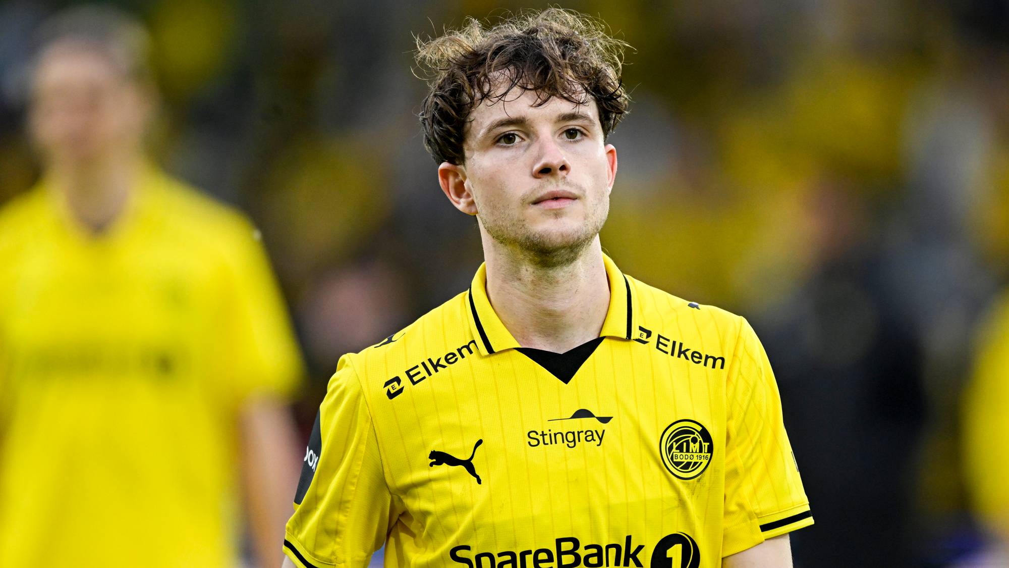 Fotballspiller fra Bodø/Glimt i gul drakt på en fotballbane. (Bildebeskrivelsen er laget av en KI-tjeneste)