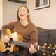 Roger Myren / NRK En ung kvinne sitter i en sofa med en gitar. Hun smiler.