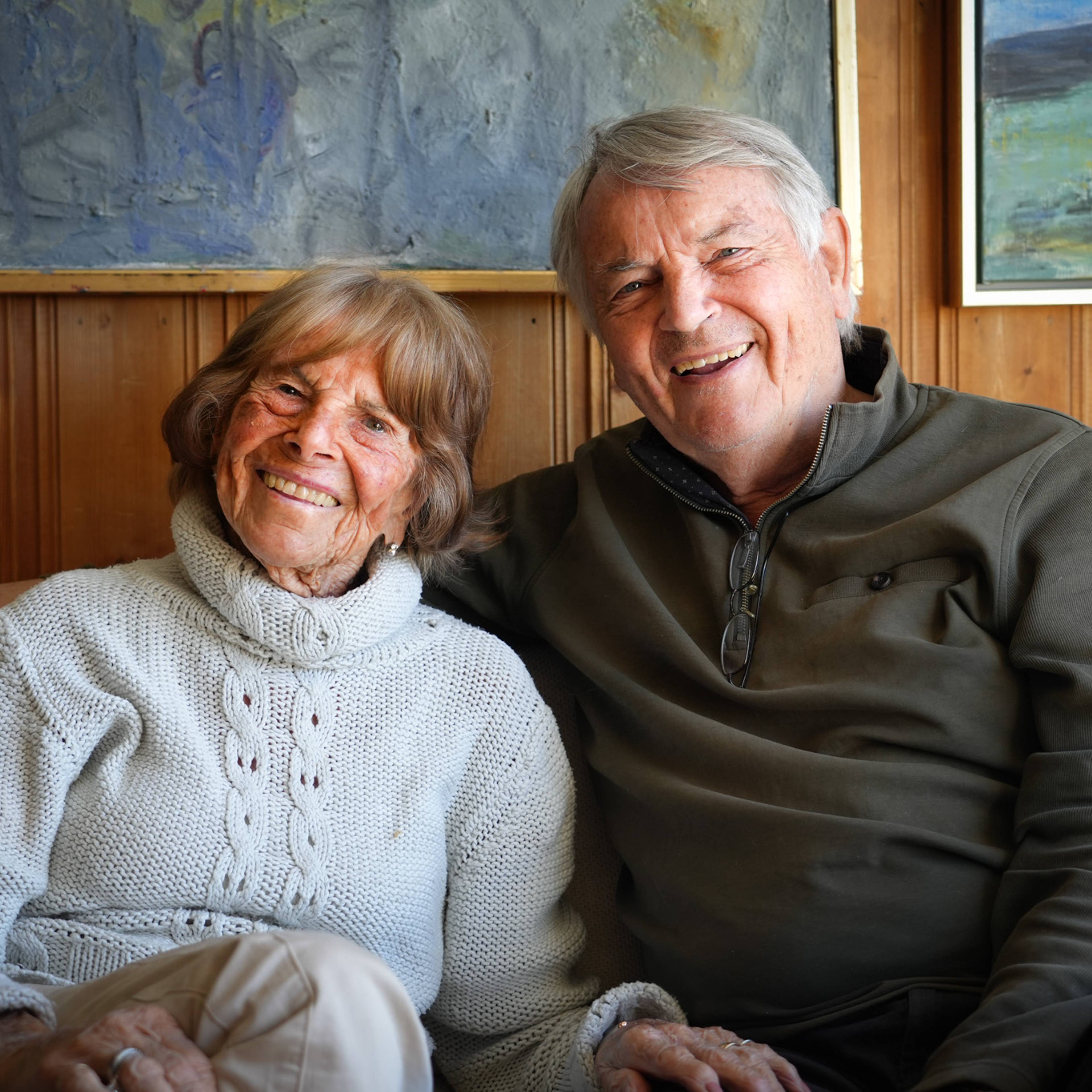 Mor og sønn sitter i sofaen og smiler mot kamera. Foran dem står et brennende stearinlys. (Bildebeskrivelsen er laget av en KI-tjeneste)