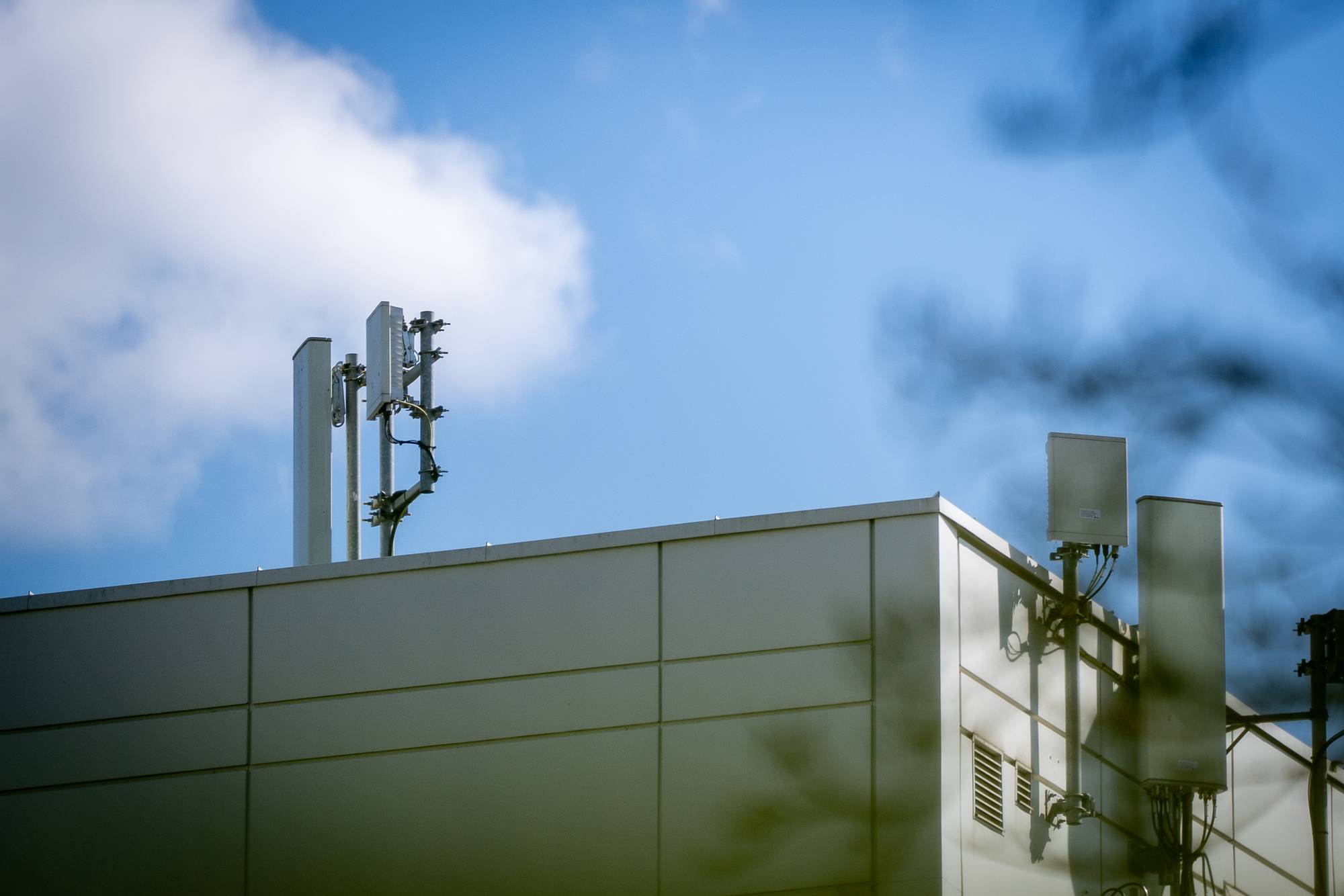 En bygning med flere antenner på taket er synlig. Antennene er festet til stolper og koblet med kabler. Det er en lys himmel med noen skyer. Bygningen er av nyere dato med store paneler. (Bildebeskrivelsen er laget av en KI-tjeneste)