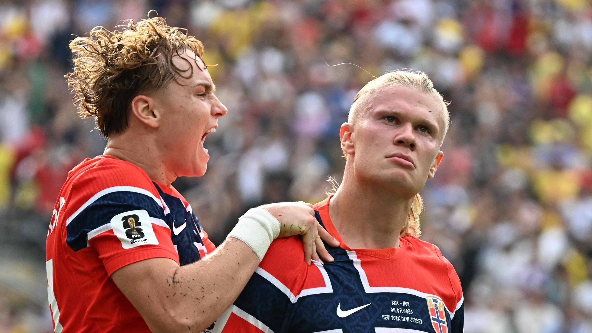 To fotballspillere i norske landslagsdrakter jubler etter en scoring på en fullsatt stadion. (Bildebeskrivelsen er laget av en KI-tjeneste)