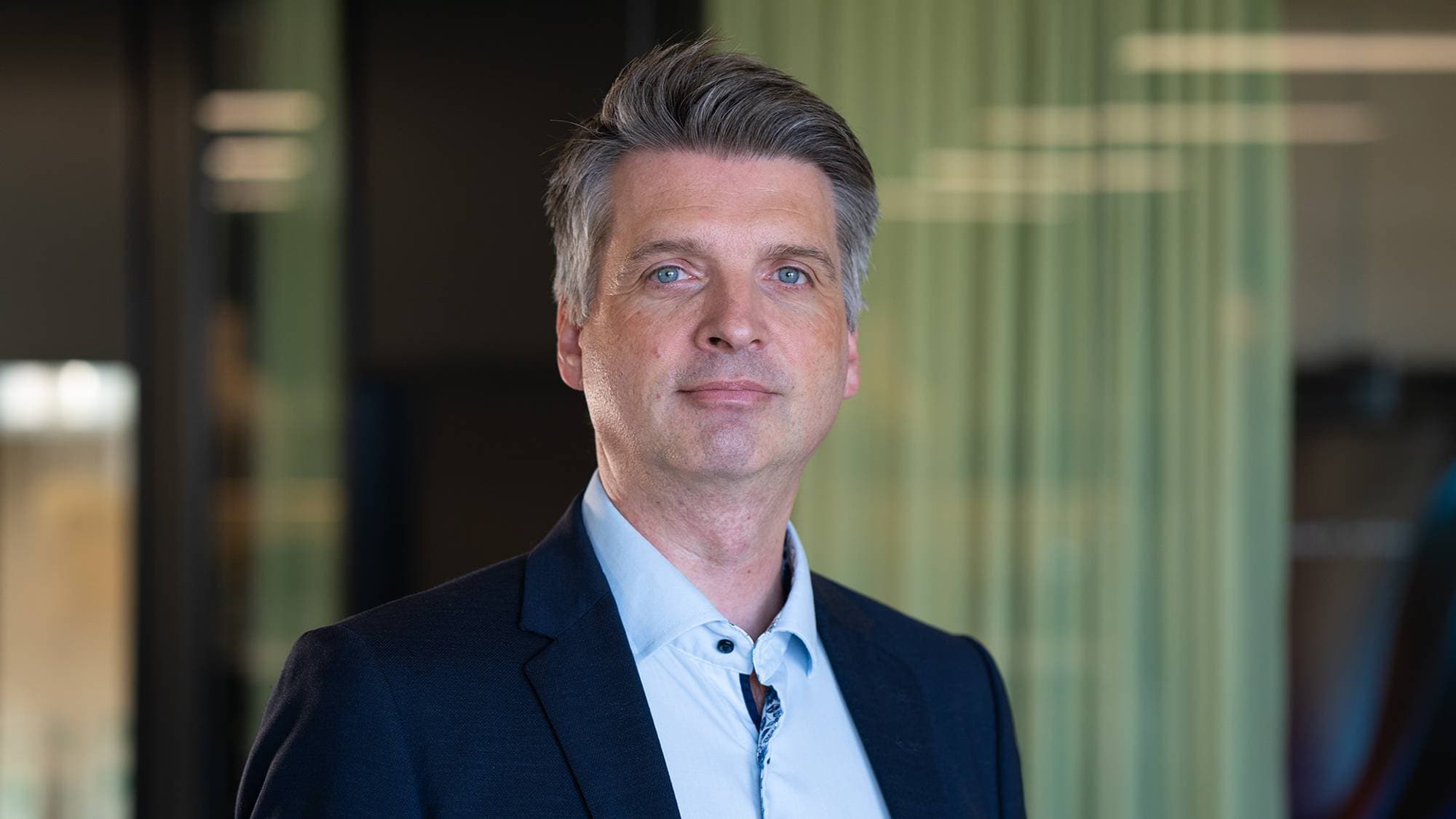 En mann i blå skjorte og blazer ser inn i kamera.