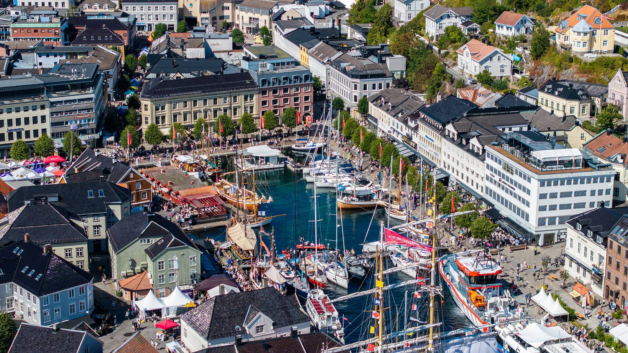 Flyfoto av Arendal gjestehavn med mange båter og folk i gatene under Arendalsuka. (Bildebeskrivelsen er laget av en KI-tjeneste)