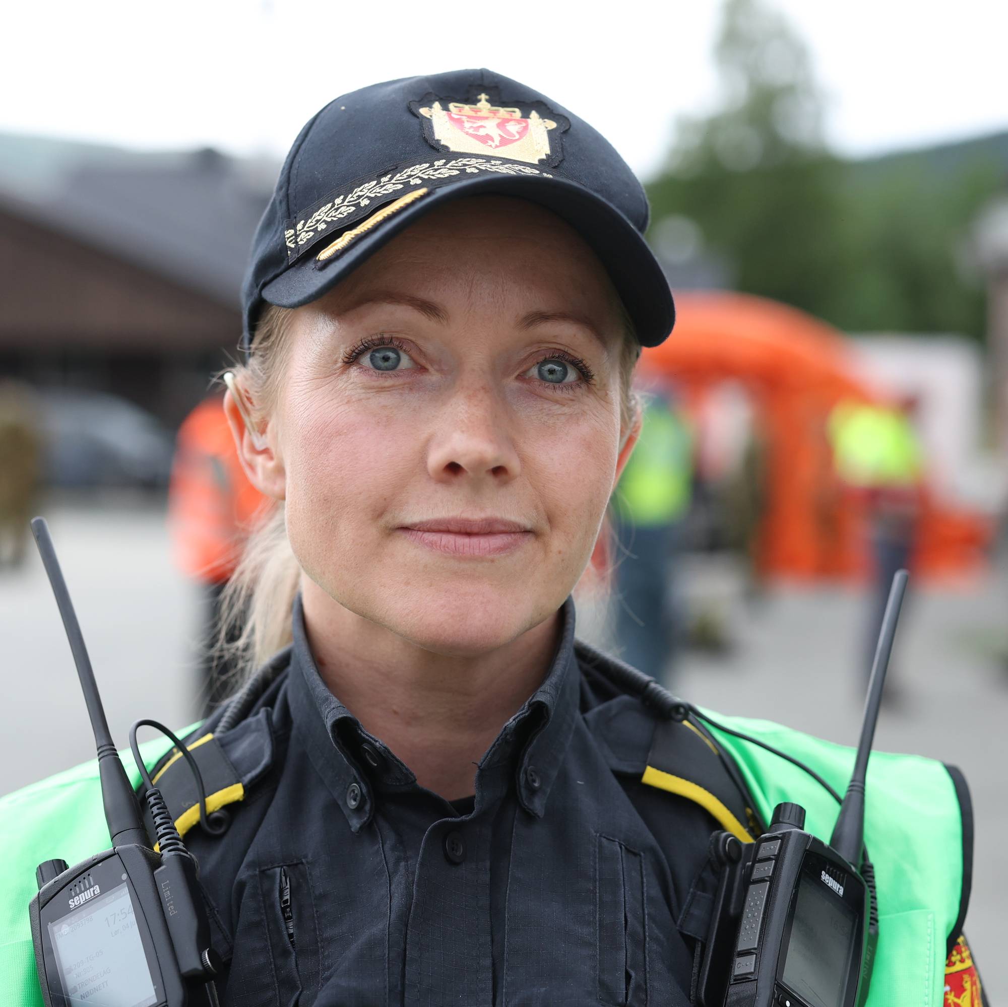 Politibetjent i uniform og refleksvest står utendørs med to samband enheter. (Bildebeskrivelsen er laget av en KI-tjeneste)