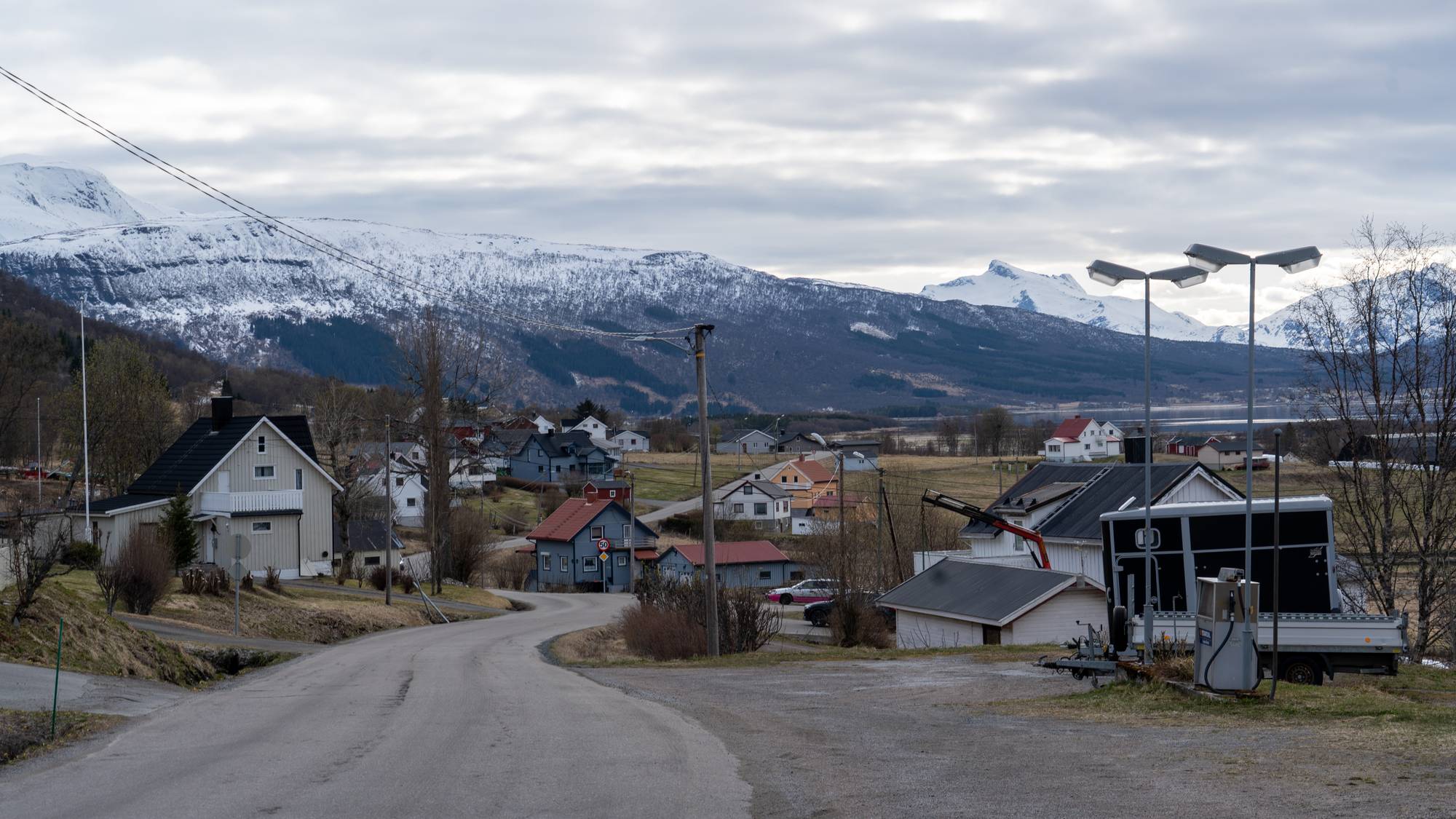 En vei med hus på hver side omringet av snødekte topper., 

