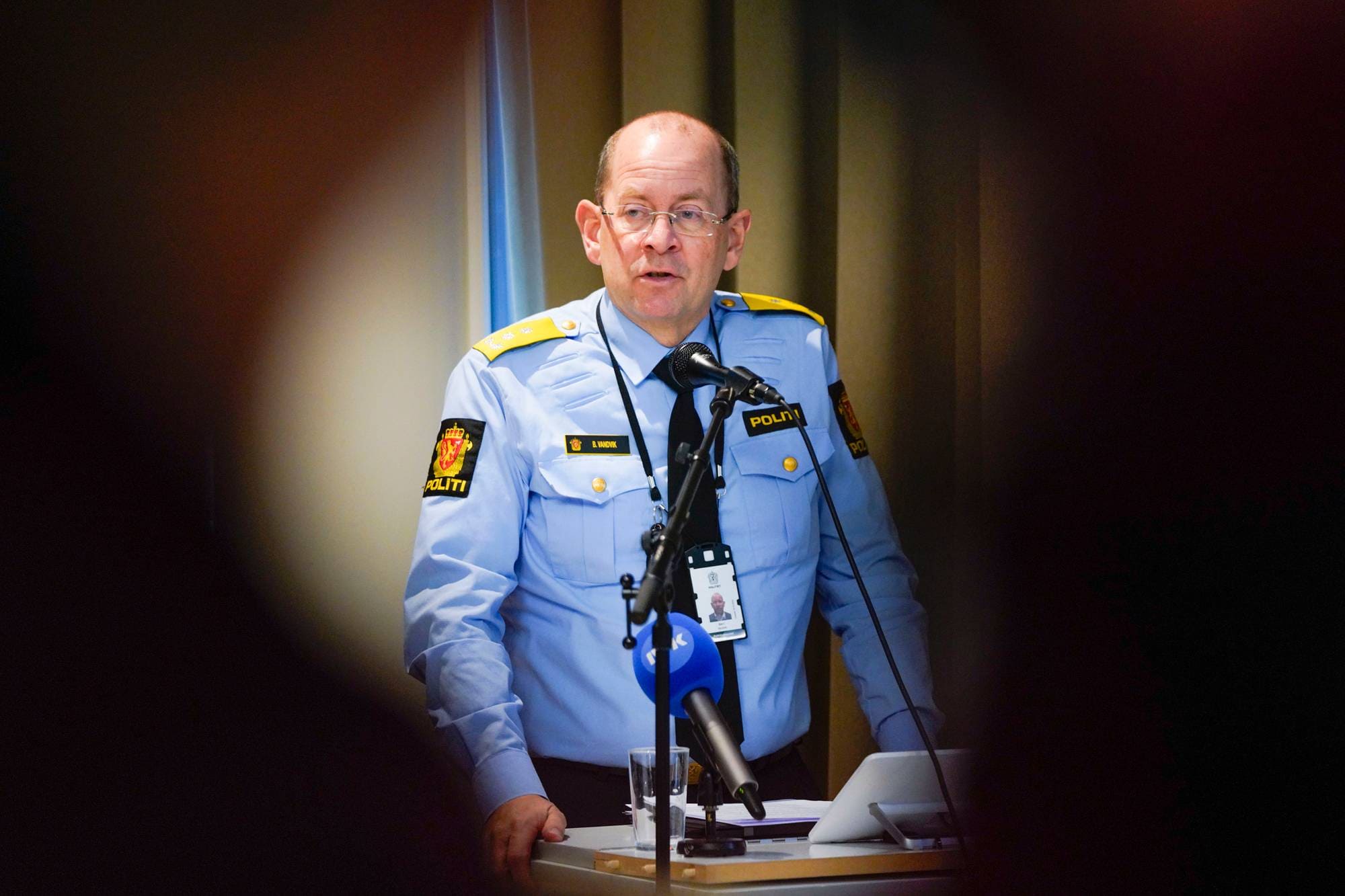 En politimann i uniform holder en tale bak en mikrofon under en pressekonferanse.