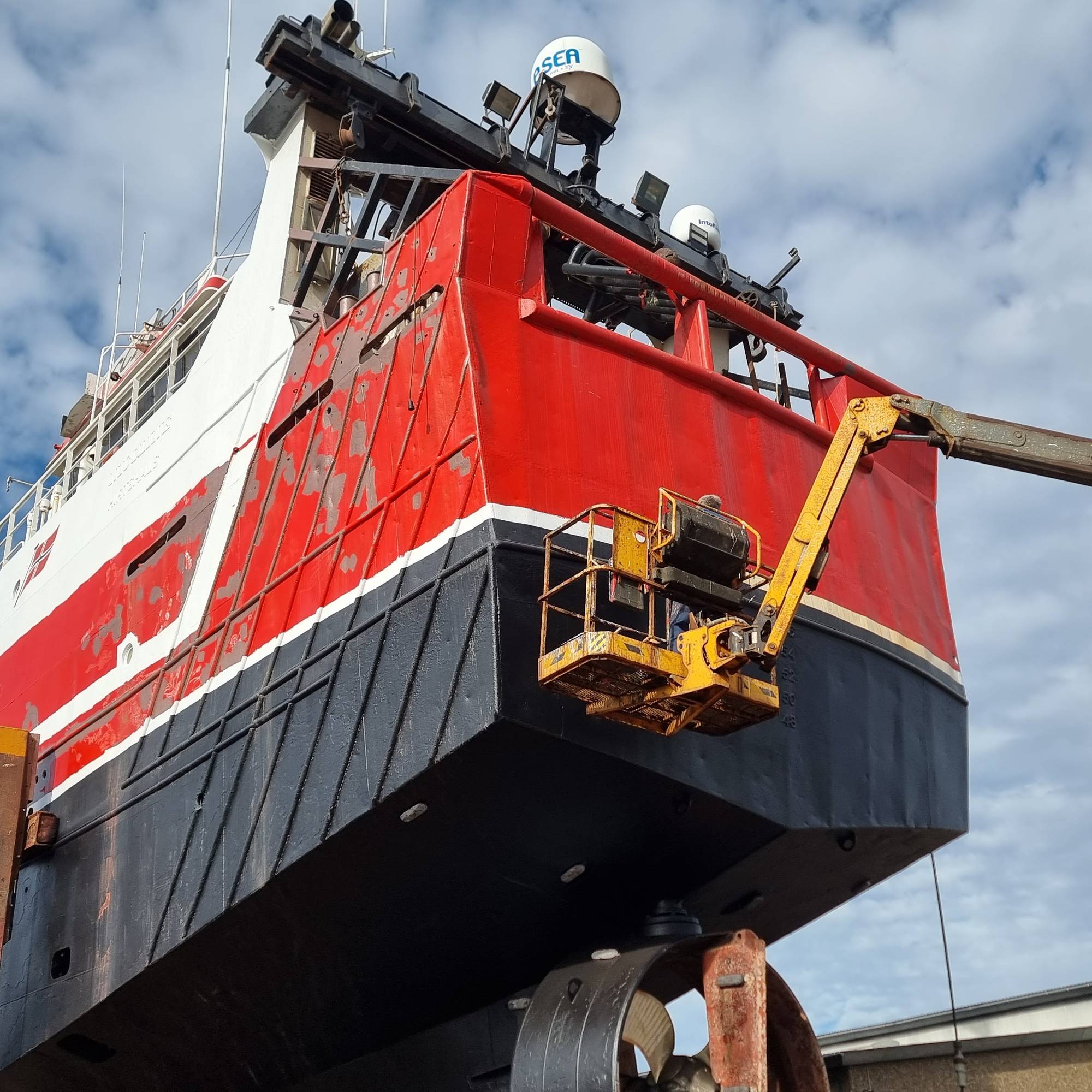Fiskebåten "Vestfjord" på dokk i Danmark. Rødt skrog og lift med folk som reparerer skader. 