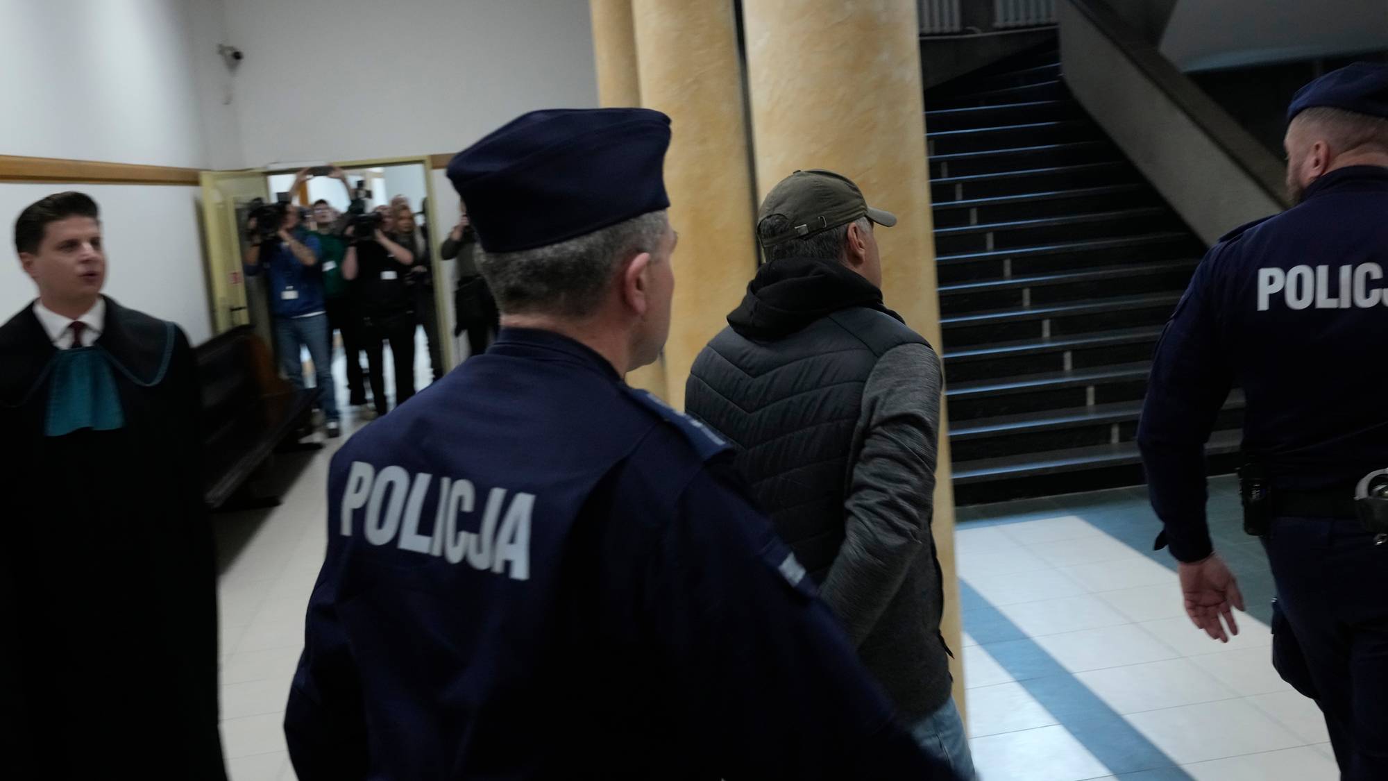 To polske politibetjenter eskorterer en mann med håndjern gjennom en bygning. (Bildebeskrivelsen er laget av en KI-tjeneste)