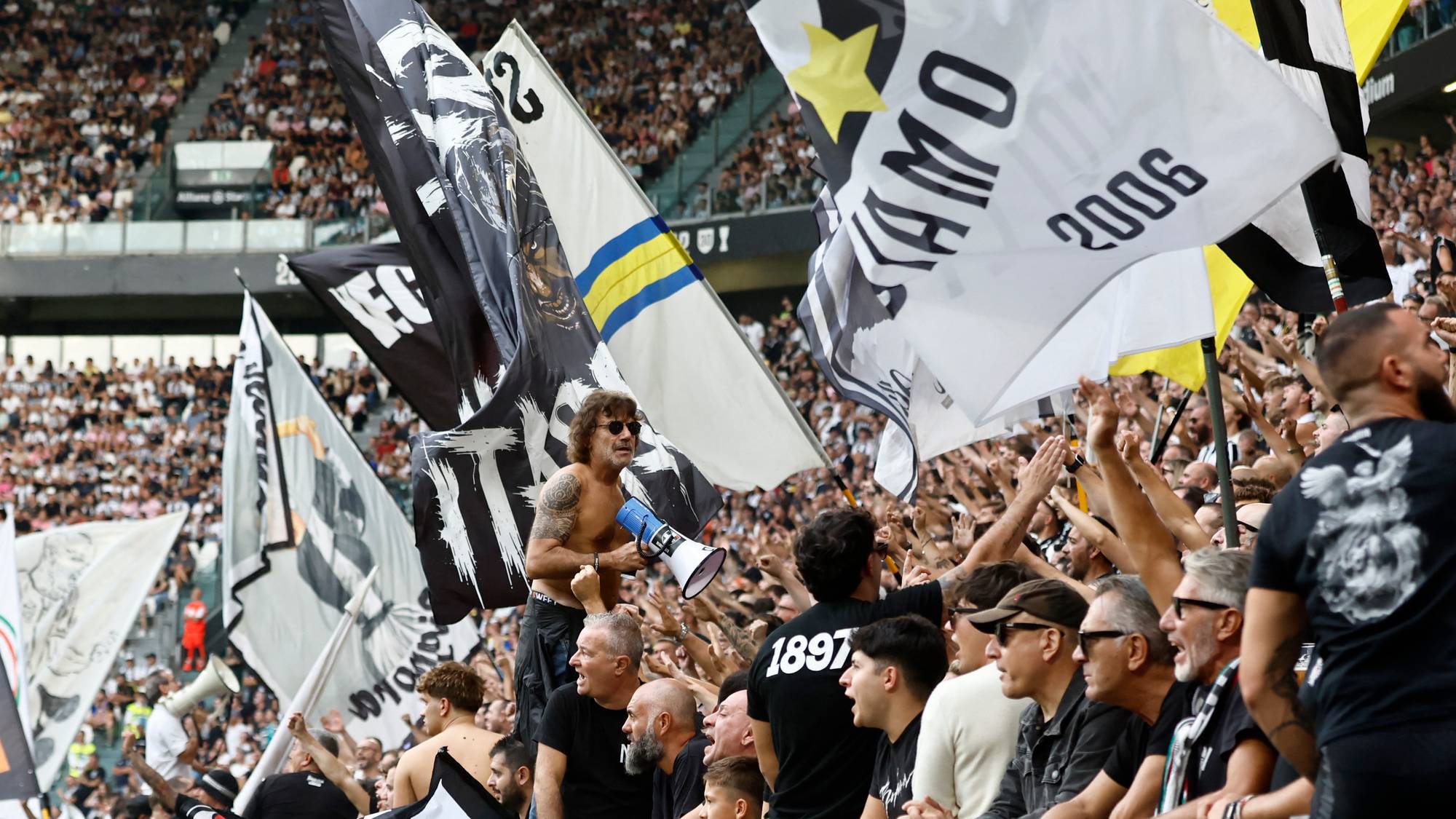 Supportere med flagg og en ropert på tribunen under en fotballkamp. (Bildebeskrivelsen er laget av en KI-tjeneste)