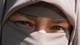 Lars Thomas Nordby / NRK Et nærbilde av en person iført niqab. Personen har grå kledning og slør som dekker ansiktet, bortsett fra øynene. I bakgrunnen er det en uskarpt hus og grønt løvverk. (Bildebeskrivelsen er laget av en KI-tjeneste)