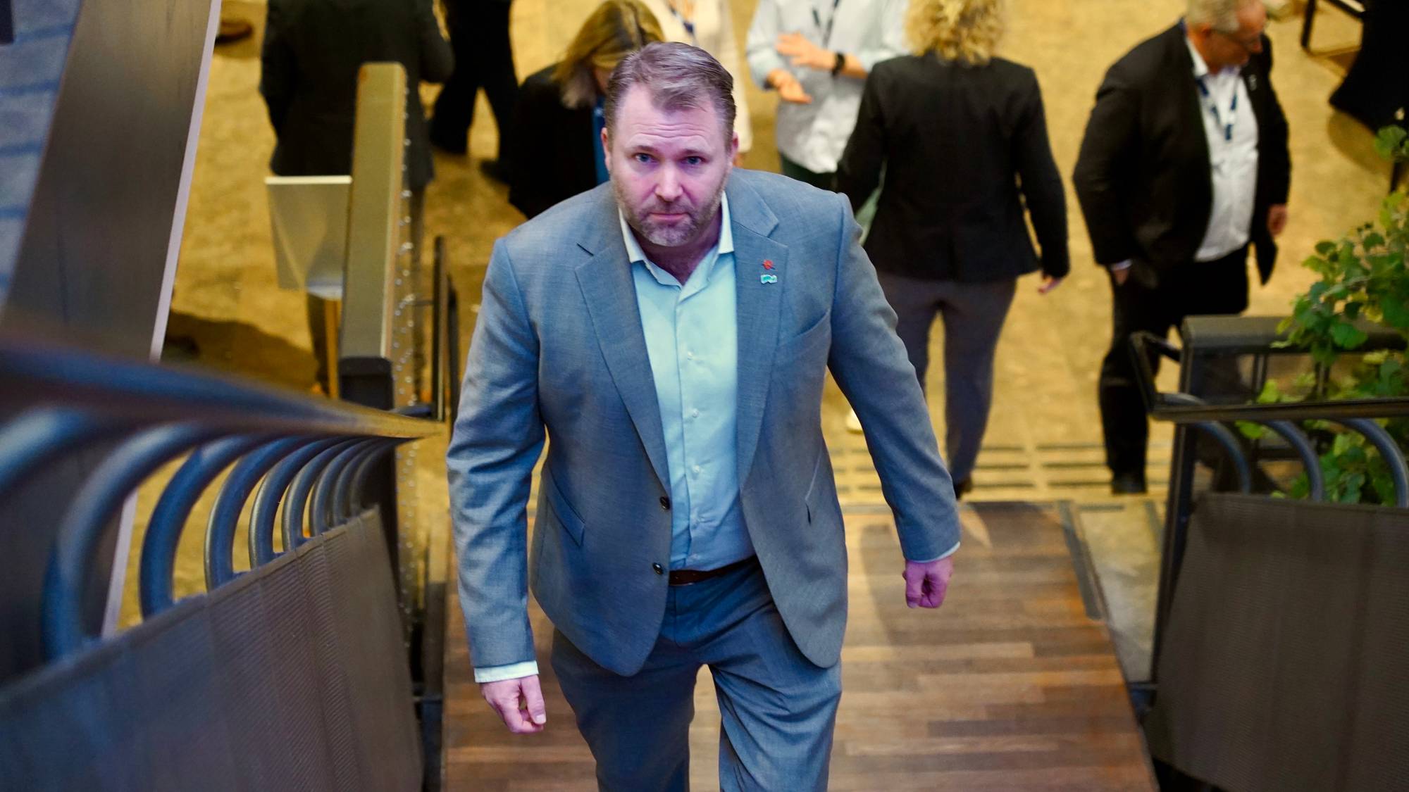 Arne Sekkelsten går opp en trapp i et lokale omgitt av andre mennesker. (Bildebeskrivelsen er laget av en KI-tjeneste)