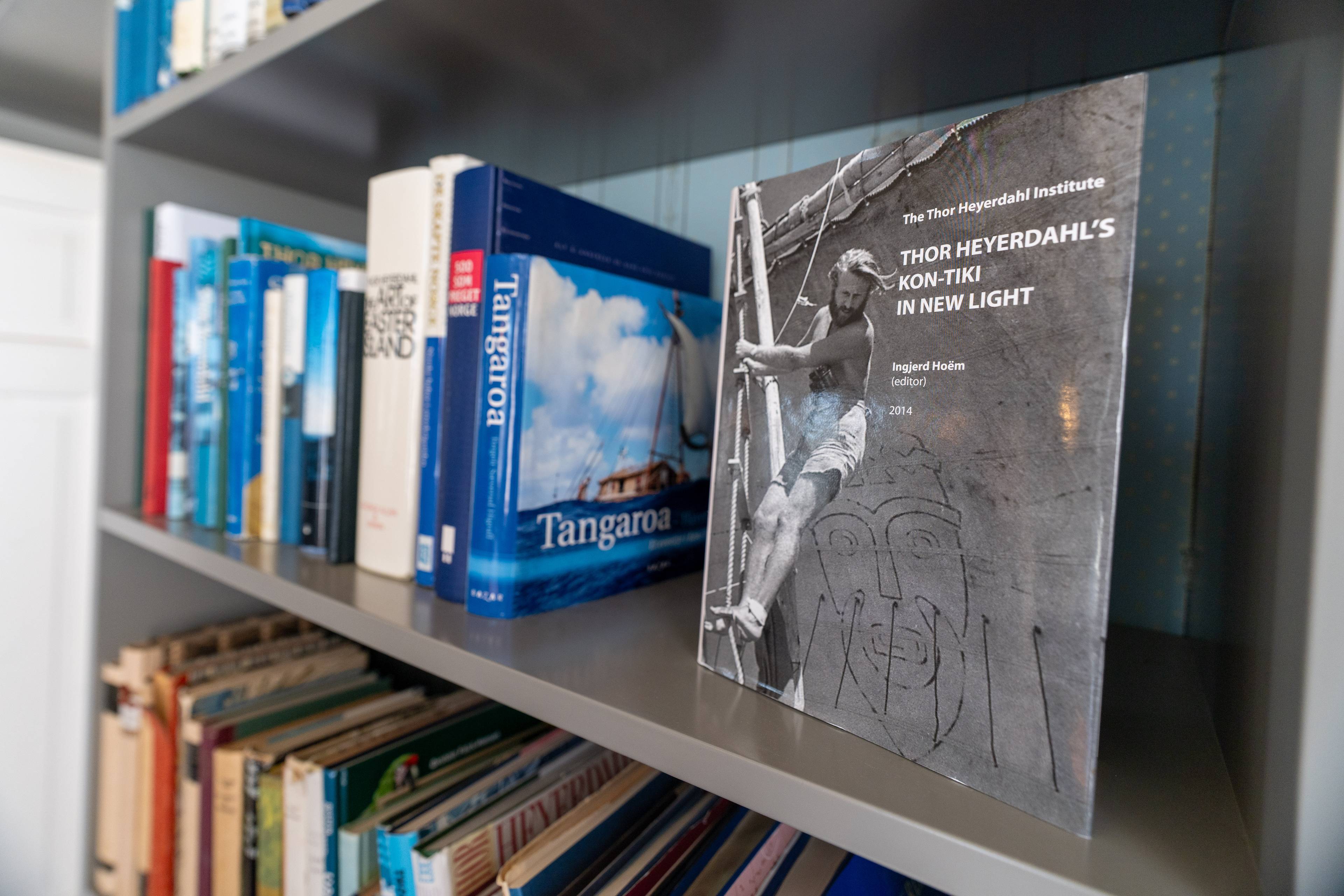 En grå bok og flere andre blå bøker står i en grå bokhylle.