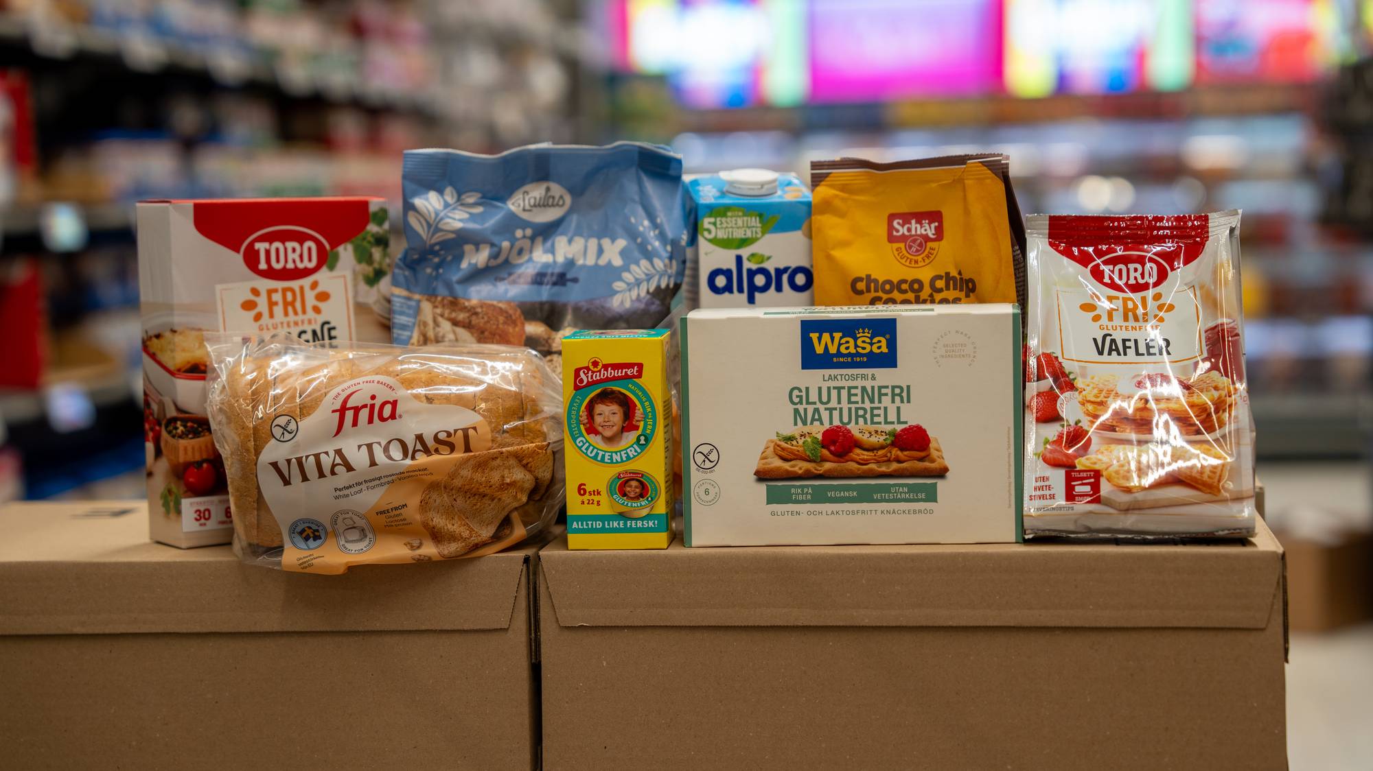 Utvalg av glutenfrie matvarer står på pappesker i en dagligvarebutikk. (Bildebeskrivelsen er laget av en KI-tjeneste)
