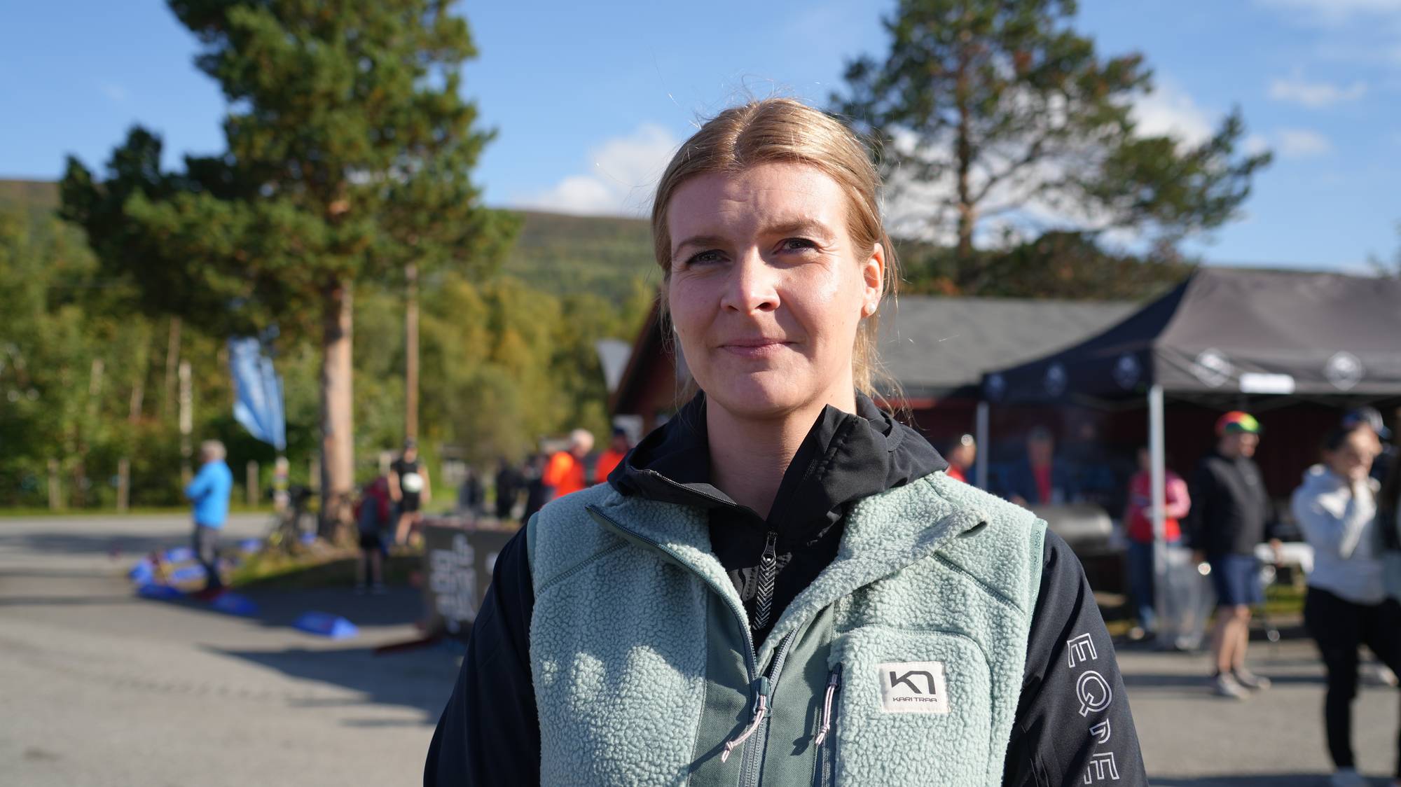 En kvinne med håret strøket bak i hestehale med grønn vest. 
