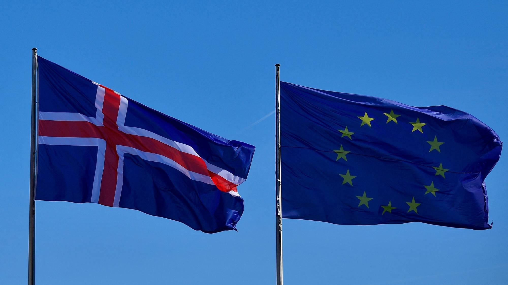 Islands og EUs flagg vaiende side om side mot en blå himmel. (Bildebeskrivelsen er laget av en KI-tjeneste)