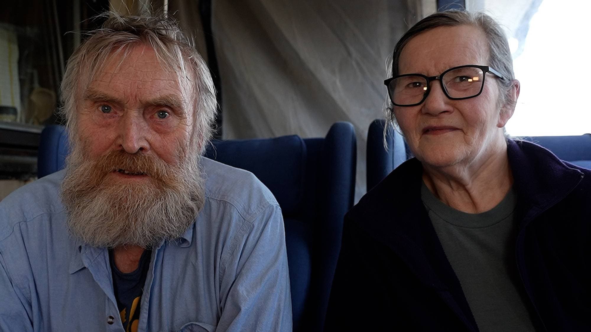 En eldre mann med skjegg og en eldre kvinne med briller sitter ved et bord innendørs. (Bildebeskrivelsen er laget av en KI-tjeneste)
