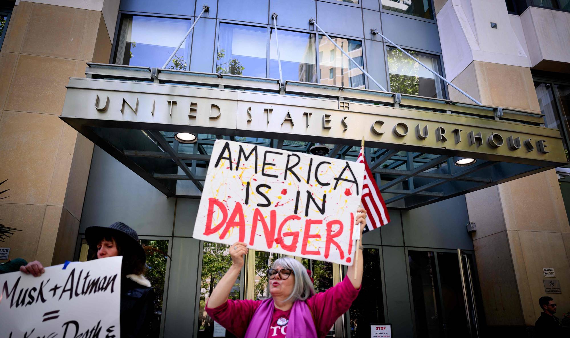 Demonstranter holder skilt foran en bygning merket United States Courthouse. En kvinne holder et skilt med teksten "AMERICA IS IN DANGER!". Et annet skilt har teksten "Musk + Altman =". (Bildebeskrivelsen er laget av en KI-tjeneste)