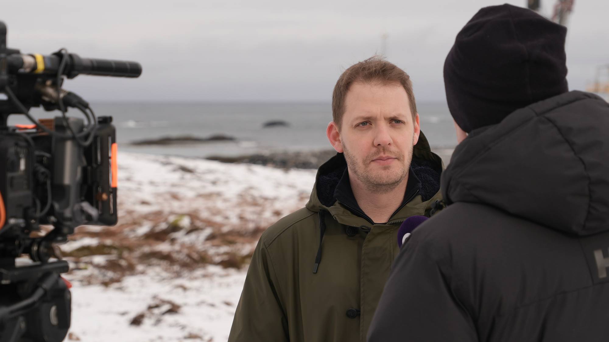 Mann blir intervjuet med havet i bakgrunnen. 