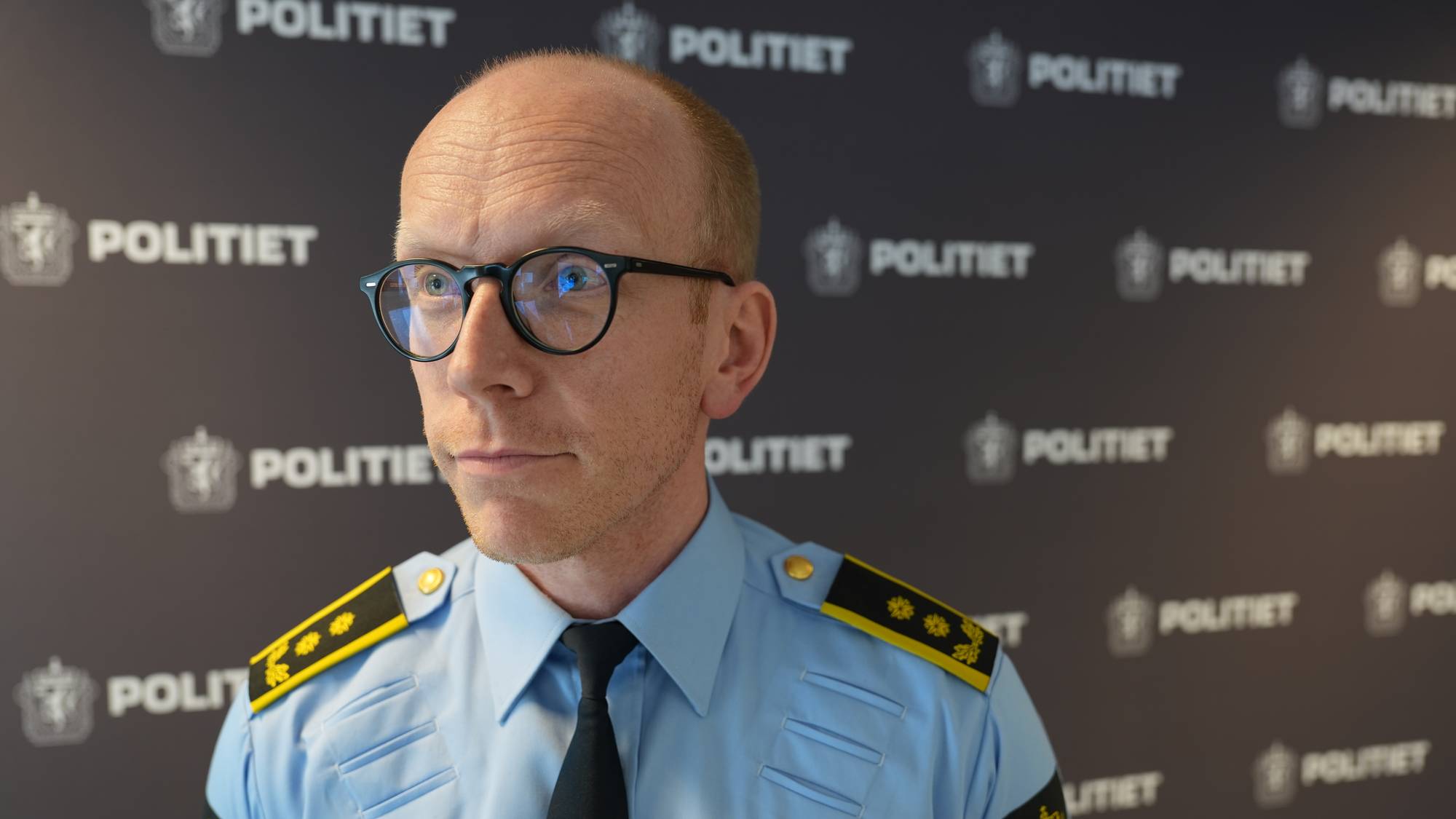 EIn mann med lite hår, runde briller og politiuniform.