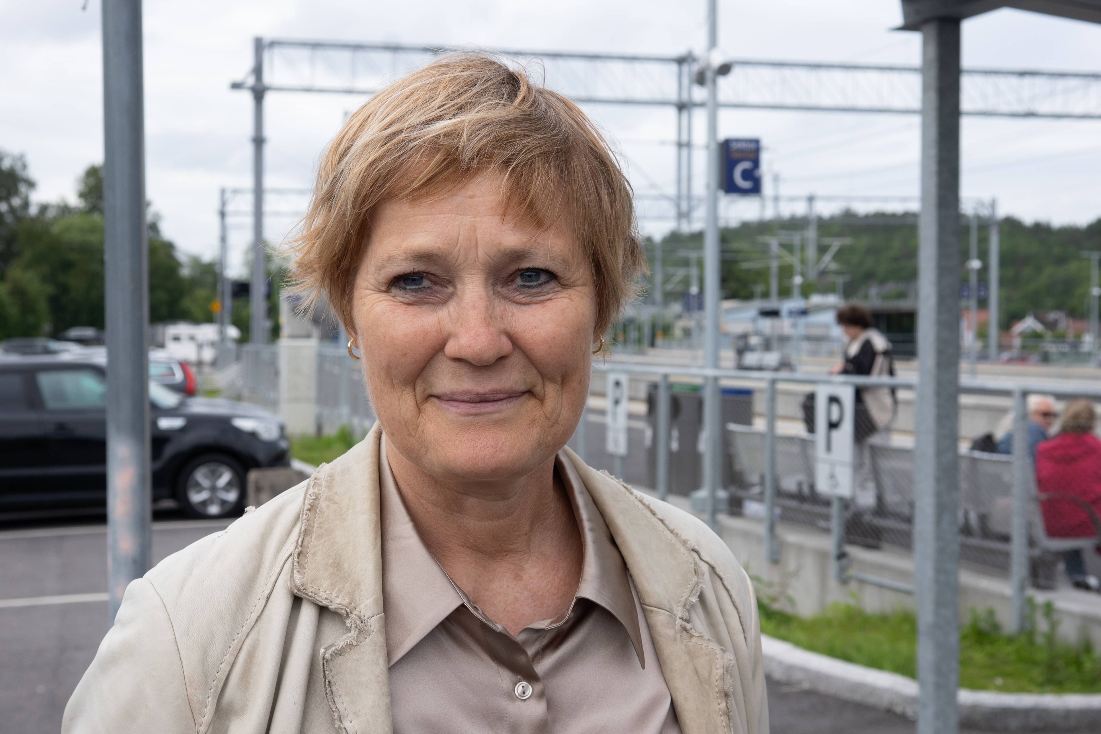 En kvinne står foran et togstopp. Hun har blondt hår og lyse klær.