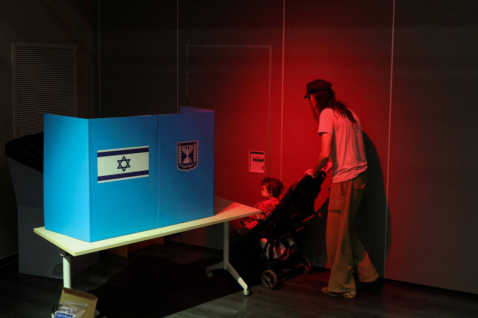 Person med barnevogn ved en israelsk valgavlukke i et rom med rødt lys. (Bildebeskrivelsen er laget av en KI-tjeneste)