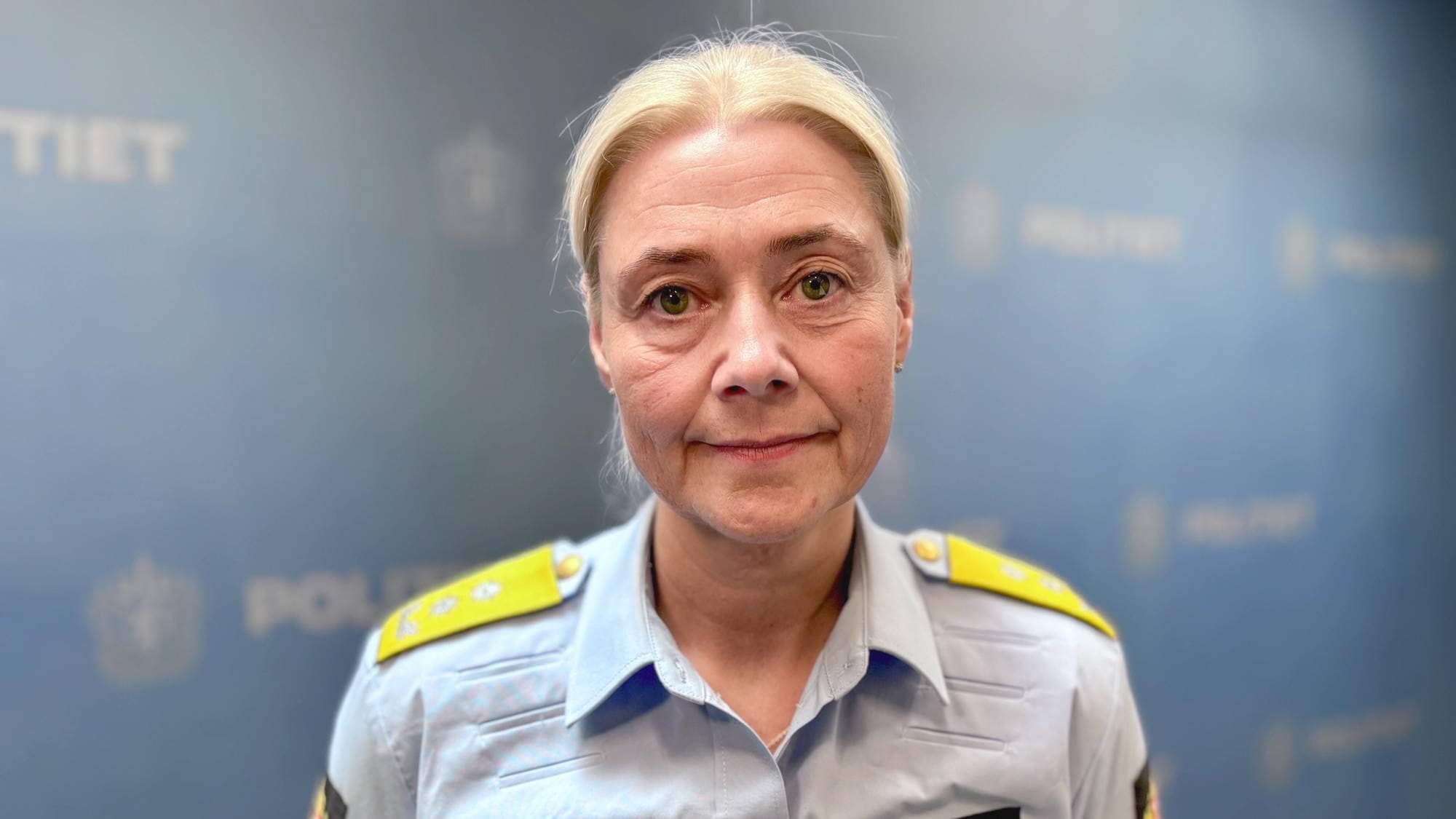 En kvinne står foran en pressevegg i politiuniform