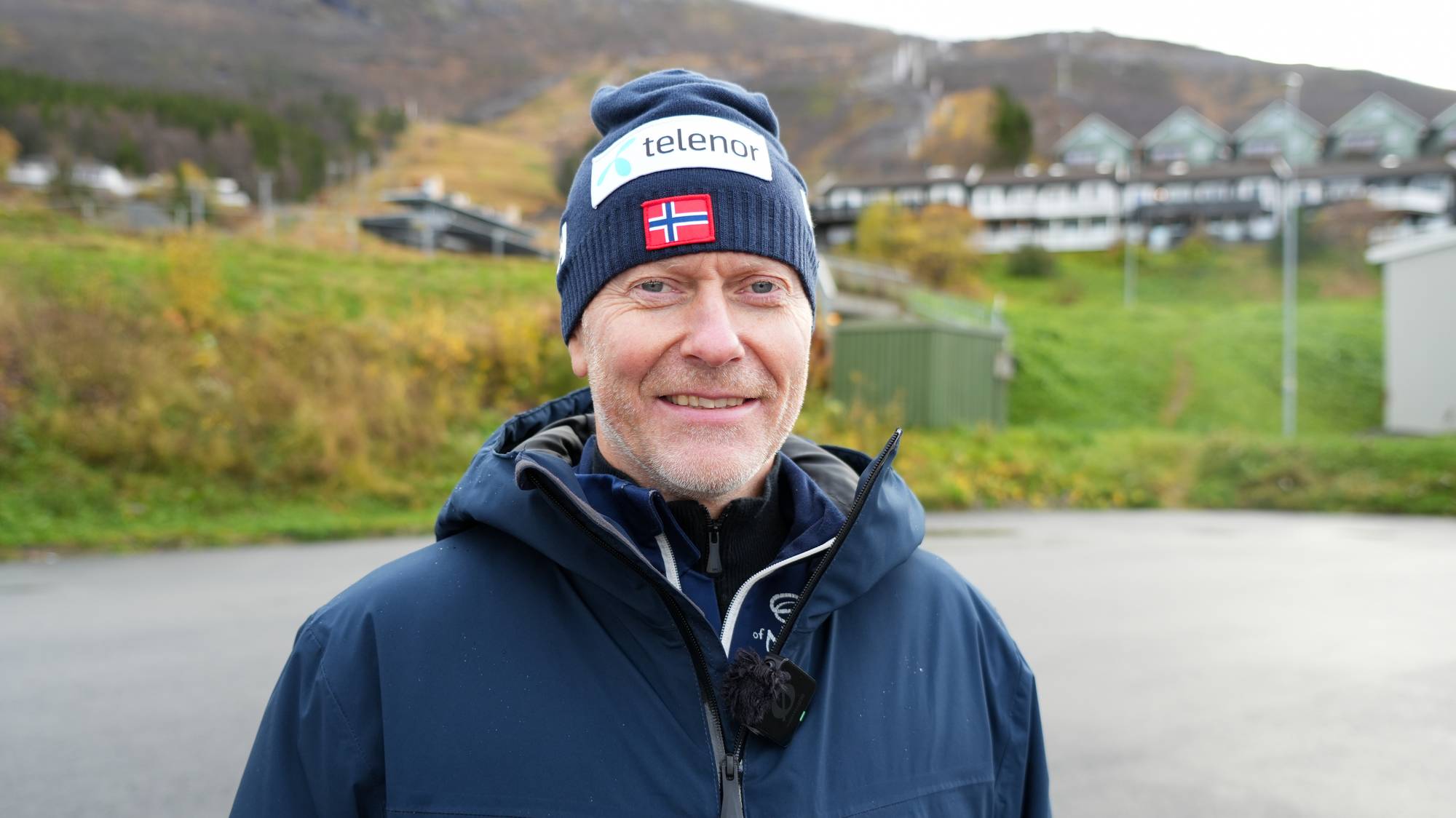 Mann med lue fra Telenor og det norske flagget utendørs foran en fjellside. (Bildebeskrivelsen er laget av en KI-tjeneste)