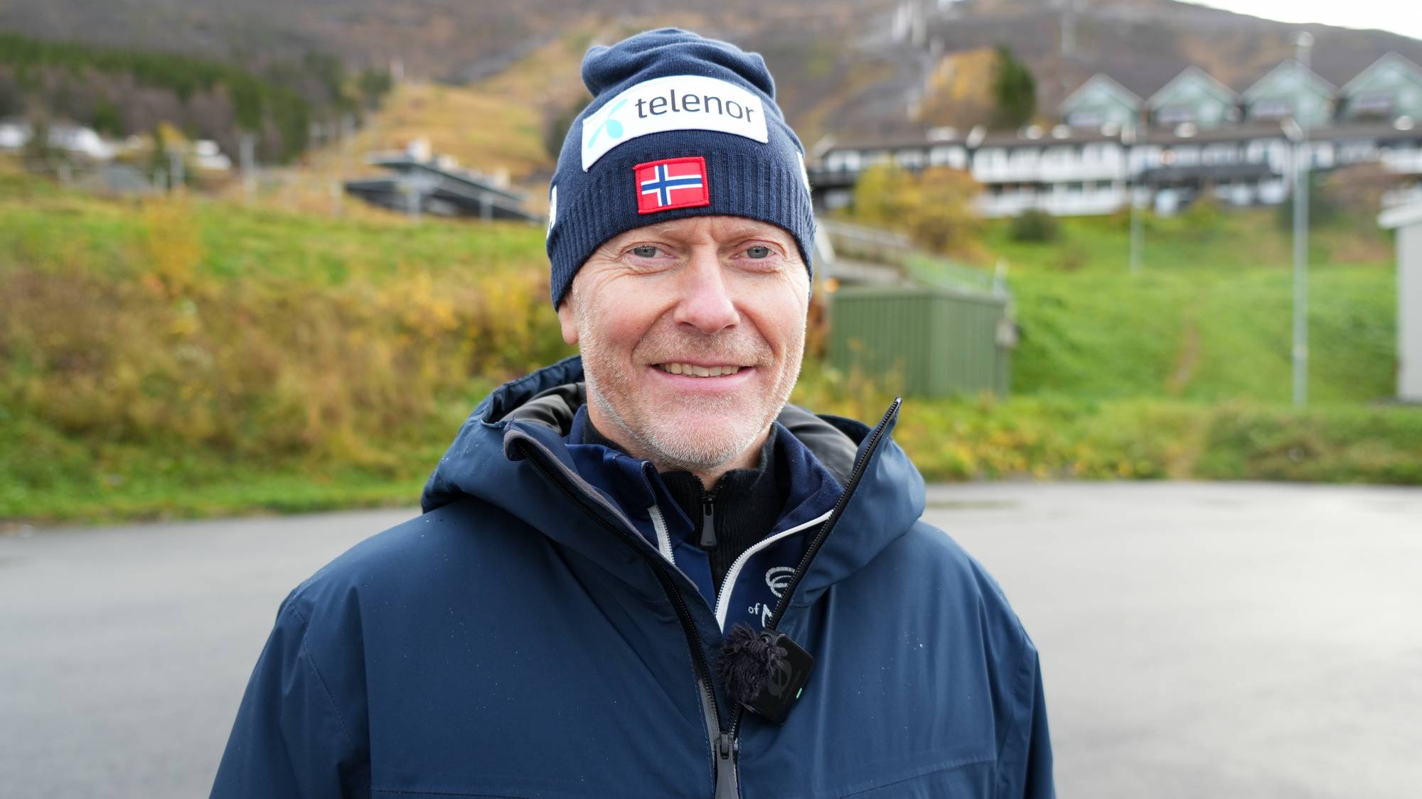 Mann med lue fra Telenor og det norske flagget utendørs foran en fjellside. (Bildebeskrivelsen er laget av en KI-tjeneste)