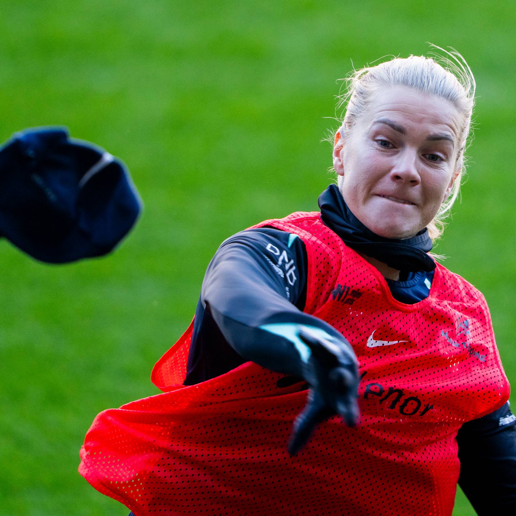 Fotballspiller i rød vest kaster en mørk genser fra seg under en treningsøkt på gressbane. (Bildebeskrivelsen er laget av en KI-tjeneste)