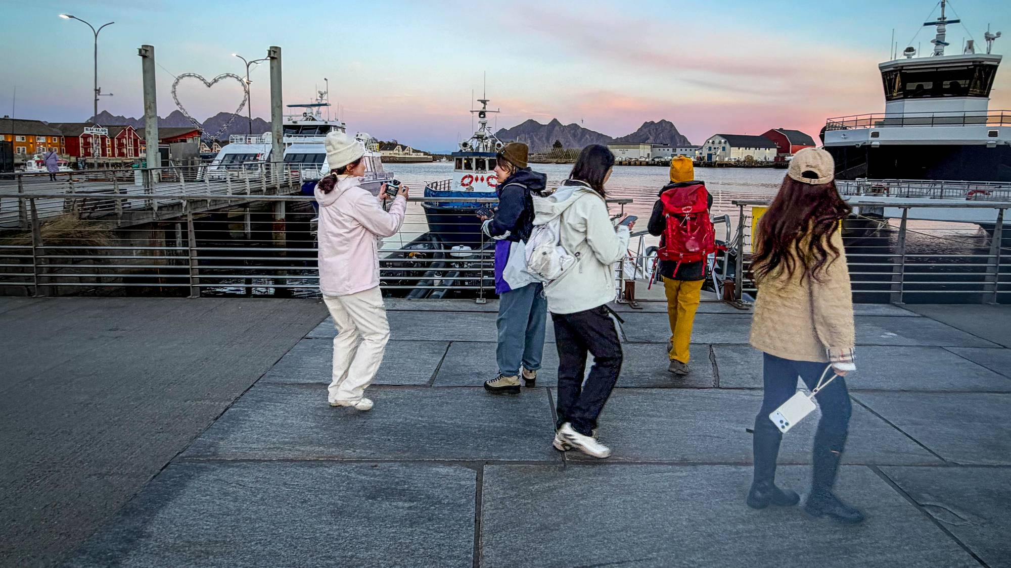 Turister på kaia i Svolvær som tar bilder av fjell og fjord i Lofoten. 