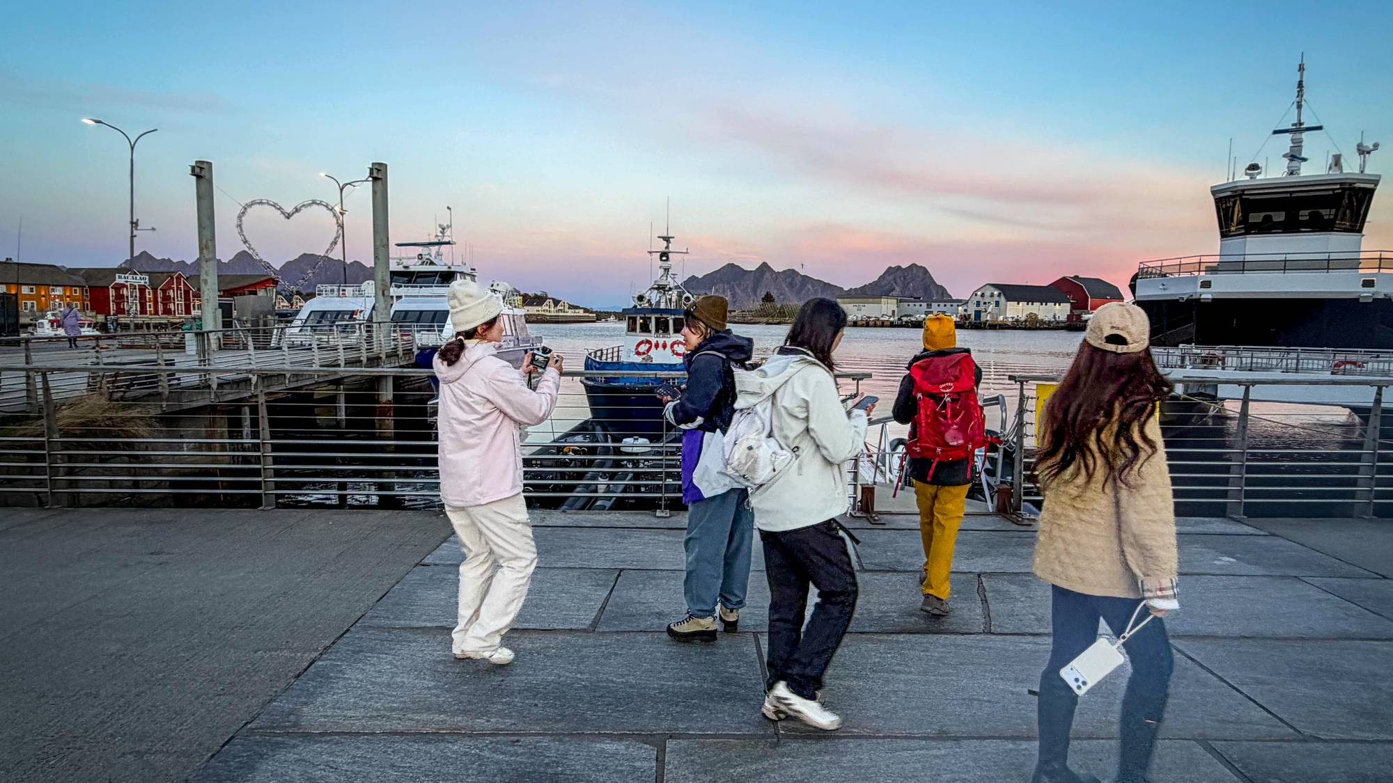 Turister på kaia i Svolvær som tar bilder av fjell og fjord i Lofoten. 