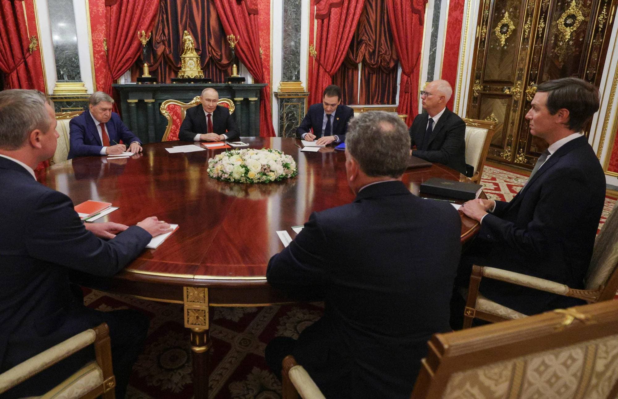 Vladimir Putin sitter ved et rundt bord med seks menn i en dekorativ sal i Kreml. (Bildebeskrivelsen er laget av en KI-tjeneste)