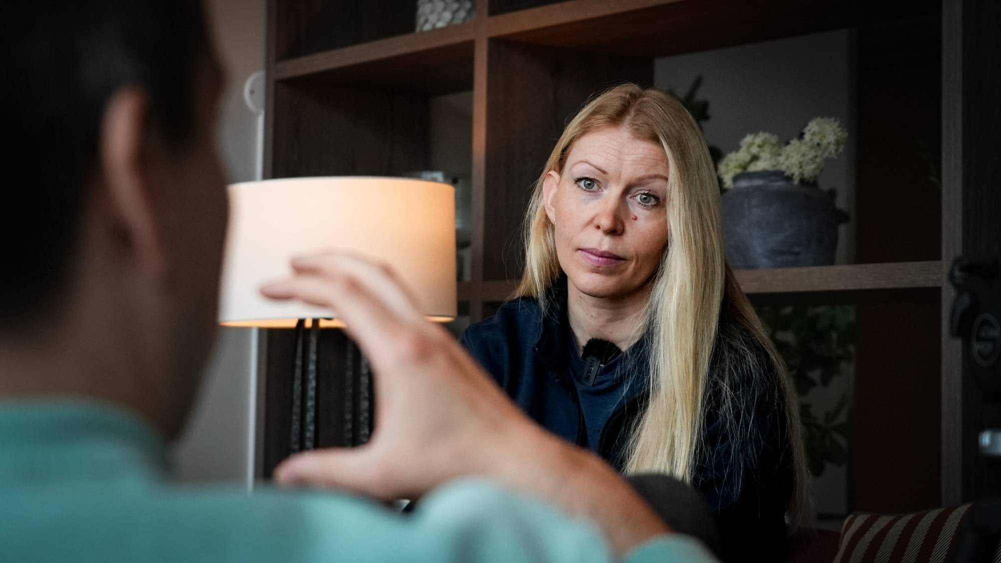 Kvinne som sitter foran en bokhylle og prater. 