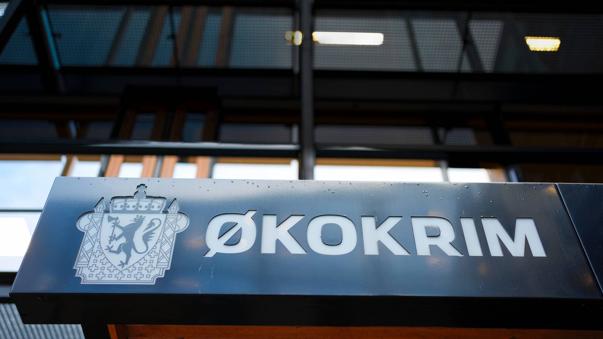 Et skilt med teksten Økokrim og det norske riksvåpenet. Bygningen bak er mørk og moderne. En vannmerke med NTB står over bildet. (Bildebeskrivelsen er laget av en KI-tjeneste)