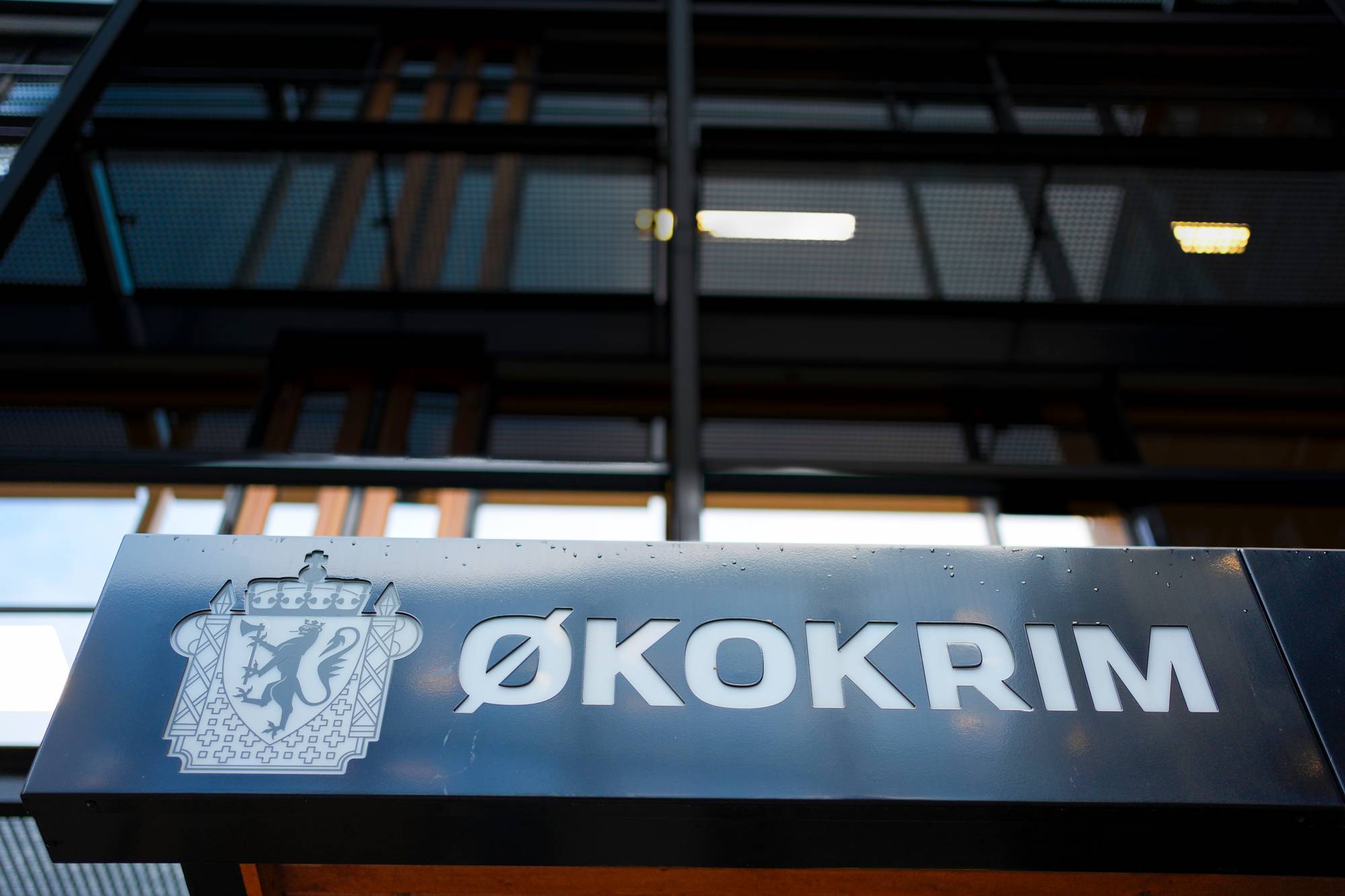 Et skilt med teksten Økokrim og det norske riksvåpenet. Bygningen bak er mørk og moderne. En vannmerke med NTB står over bildet. (Bildebeskrivelsen er laget av en KI-tjeneste)