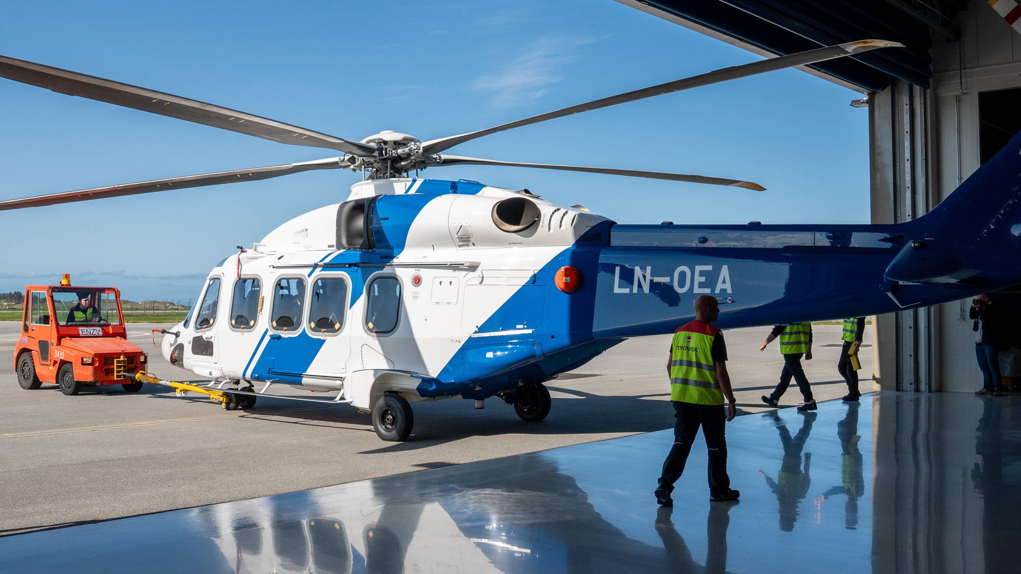 Blått og hvitt helikopter på vei ut av hangaren.