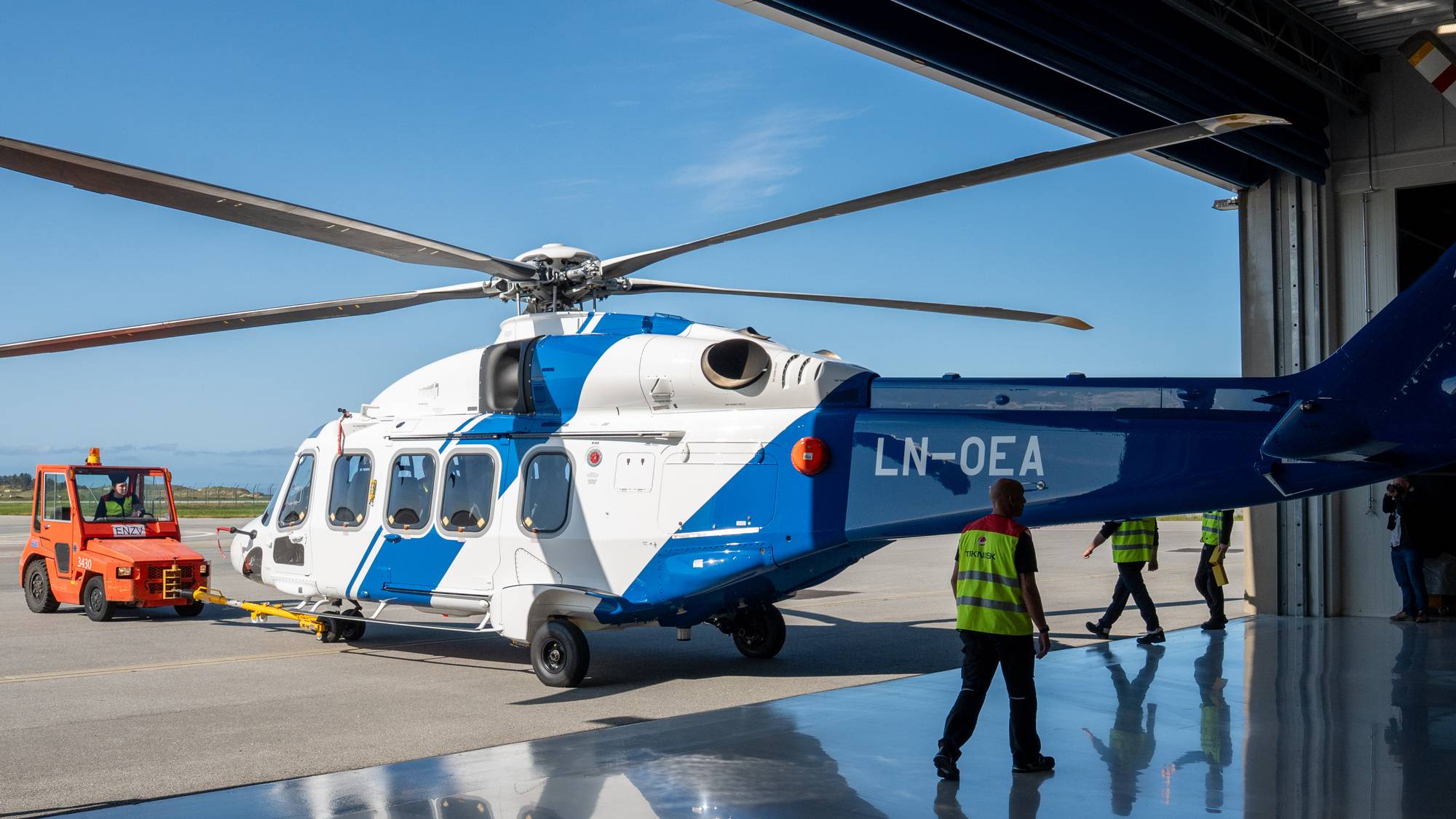 Blått og hvitt helikopter på vei ut av hangaren.
