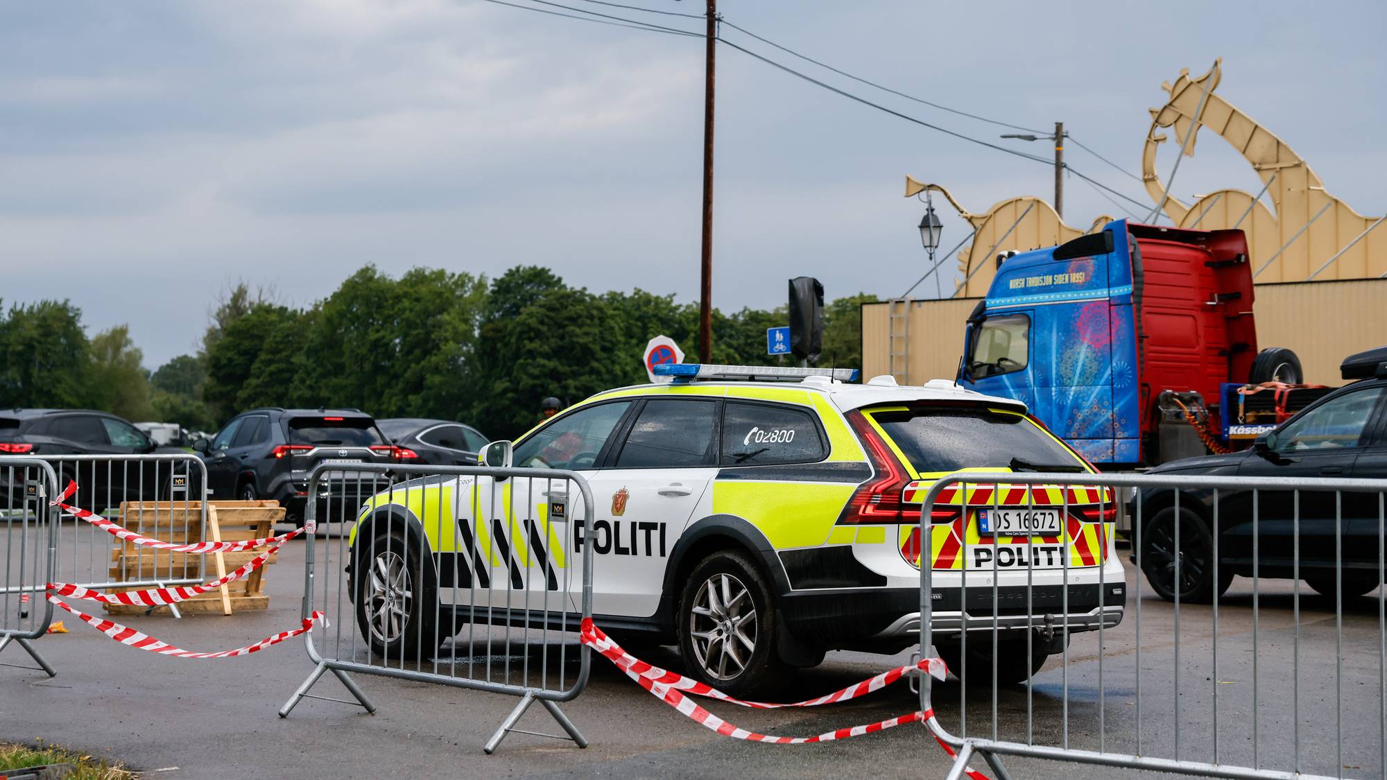 En politibil står parkert bak sperregjerder ved et område med flere kjøretøy.