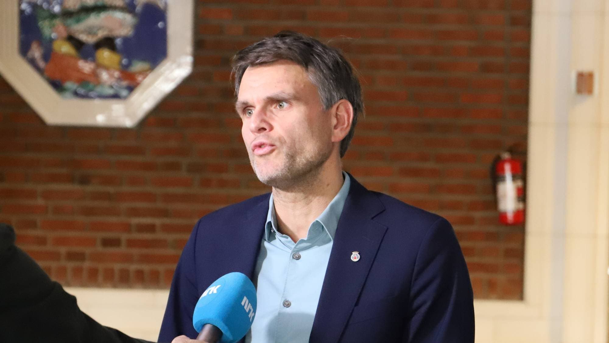 En mann i blå dressjakke og lys blå skjorte snakker til en journalist med NRK-mikrofon på rådhuset i Oslo
