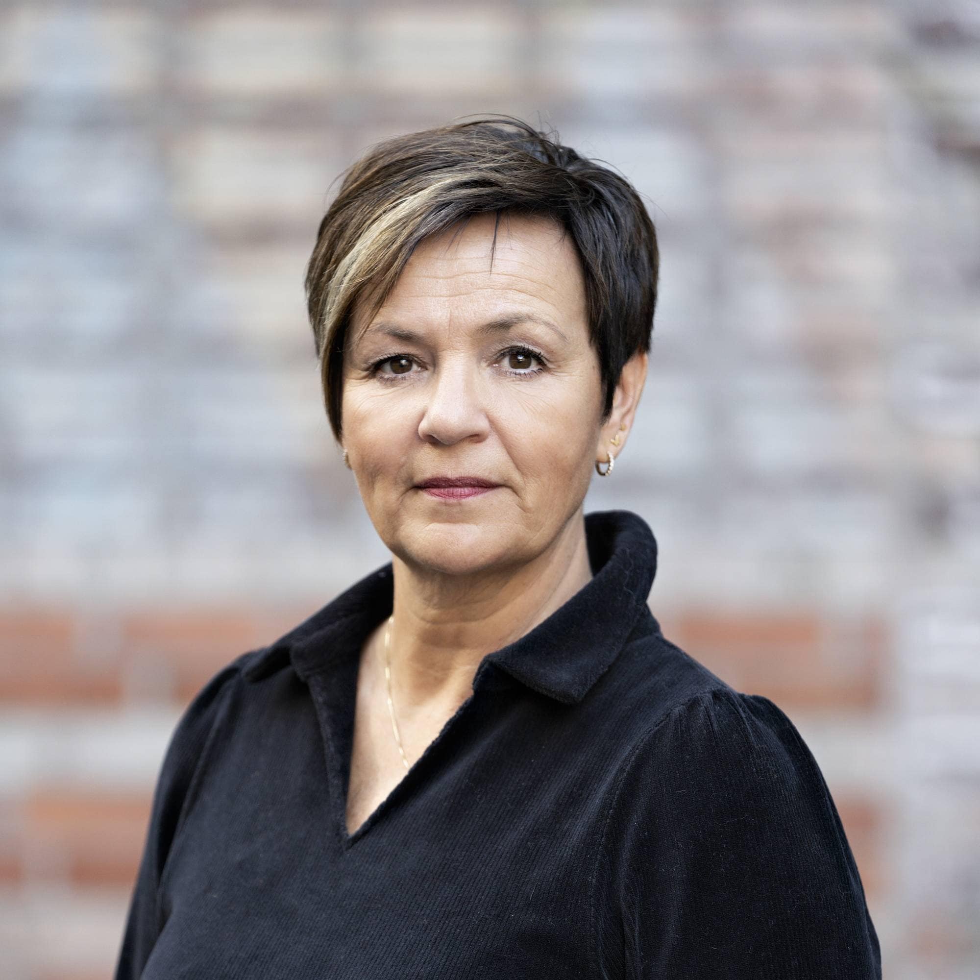 En kvinne med mørkt, kort hår og svart bluse ser inn i kamera.