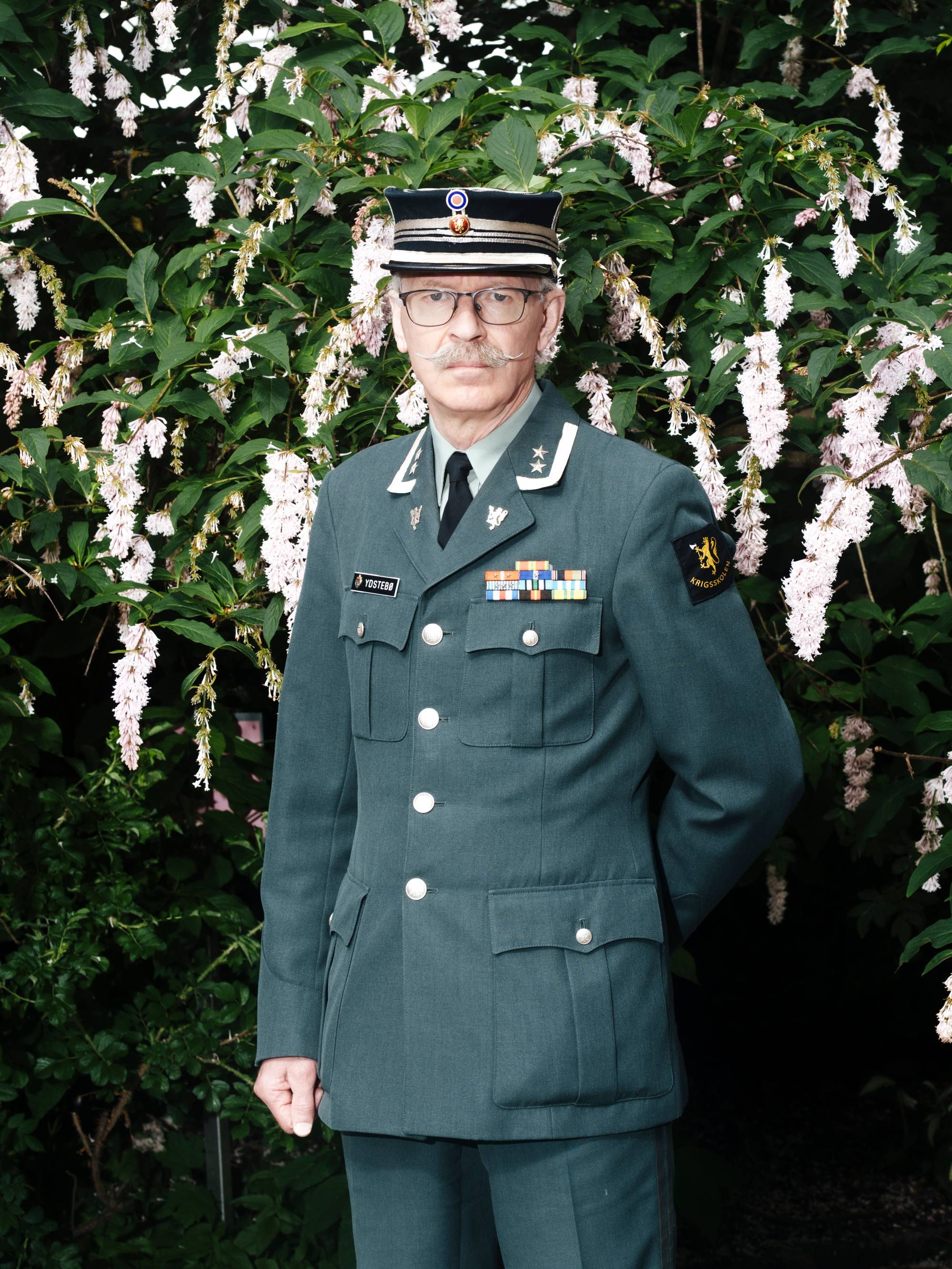 bilde av mann i militær uniform foran syriner. 