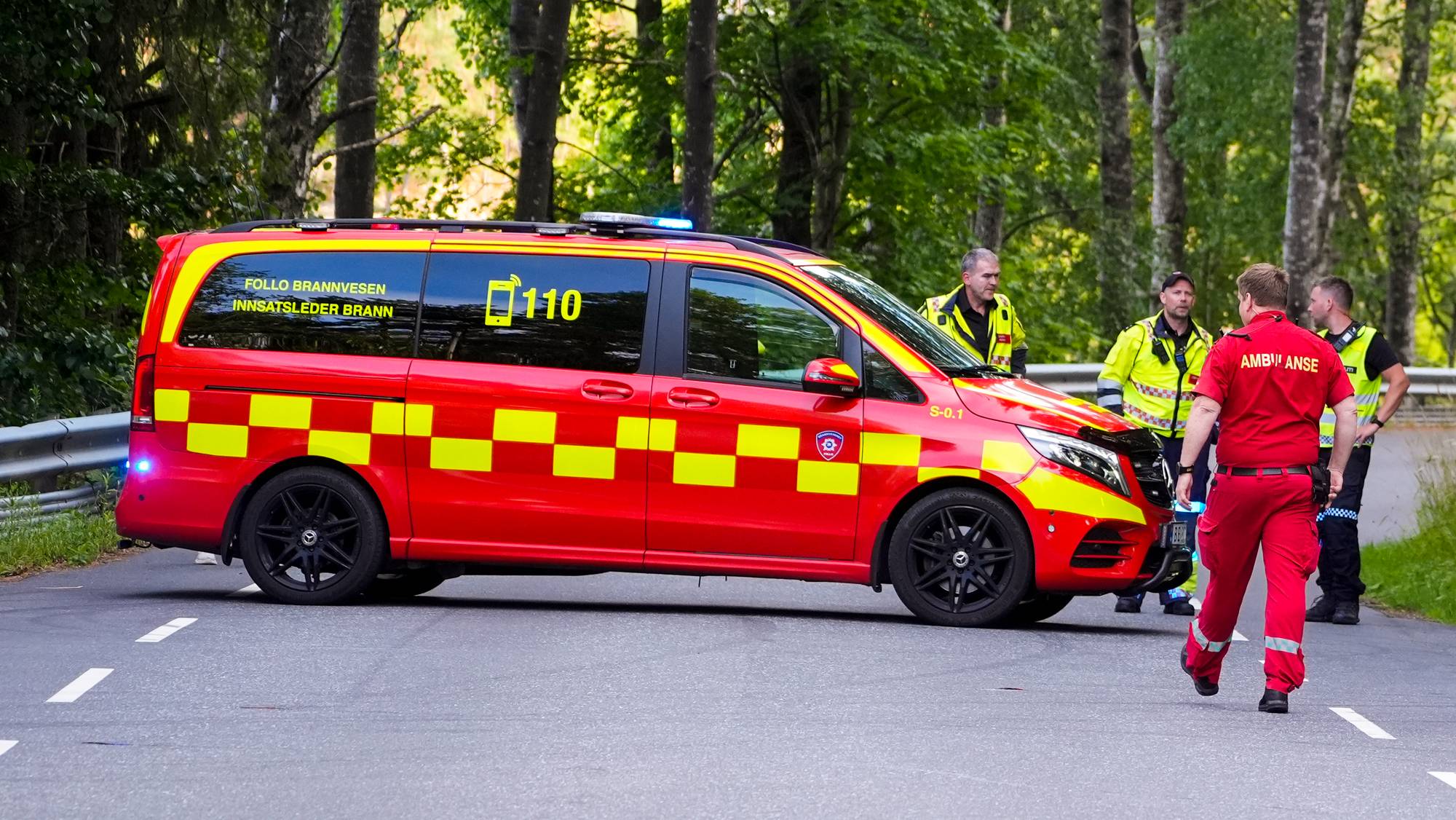 Nødetater på en sperret vei i skogen. Brannvesen og ambulansepersonell er til stede ved ulykkessted. (Bildebeskrivelsen er laget av en KI-tjeneste)
