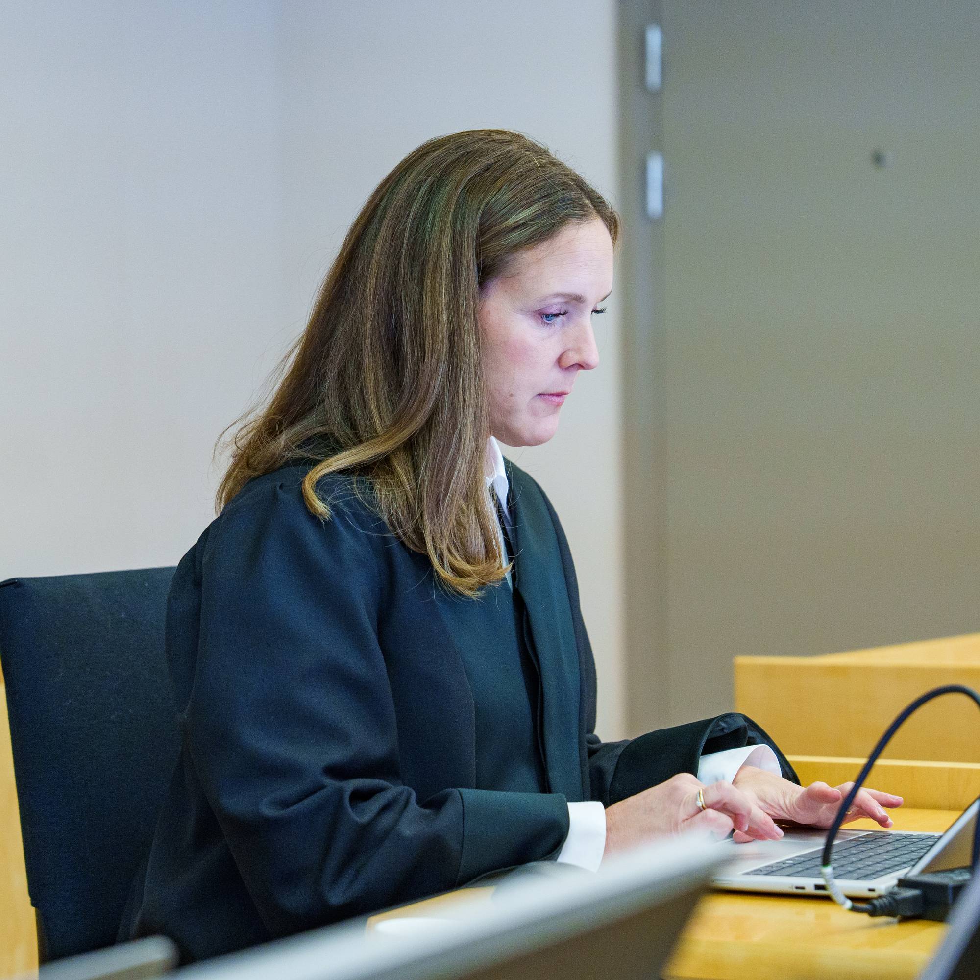 Kvinne i dommerkappe sitter ved en pult i en rettssal og skriver på en bærbar datamaskin. (Bildebeskrivelsen er laget av en KI-tjeneste)