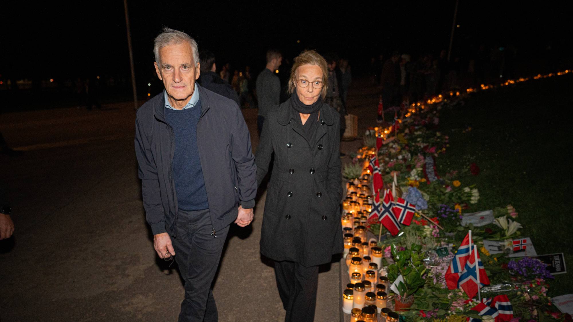 Jonas Gahr Støre og Marit Slagsvold går hånd i hånd forbi blomster og lys ved en minneplass. (Bildebeskrivelsen er laget av en KI-tjeneste)