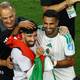 Pedro Nunes / REUTERS,NTB Algeriske fotballspillere og en trener feirer sammen på banen med et algerisk flagg. (Bildebeskrivelsen er laget av en KI-tjeneste)